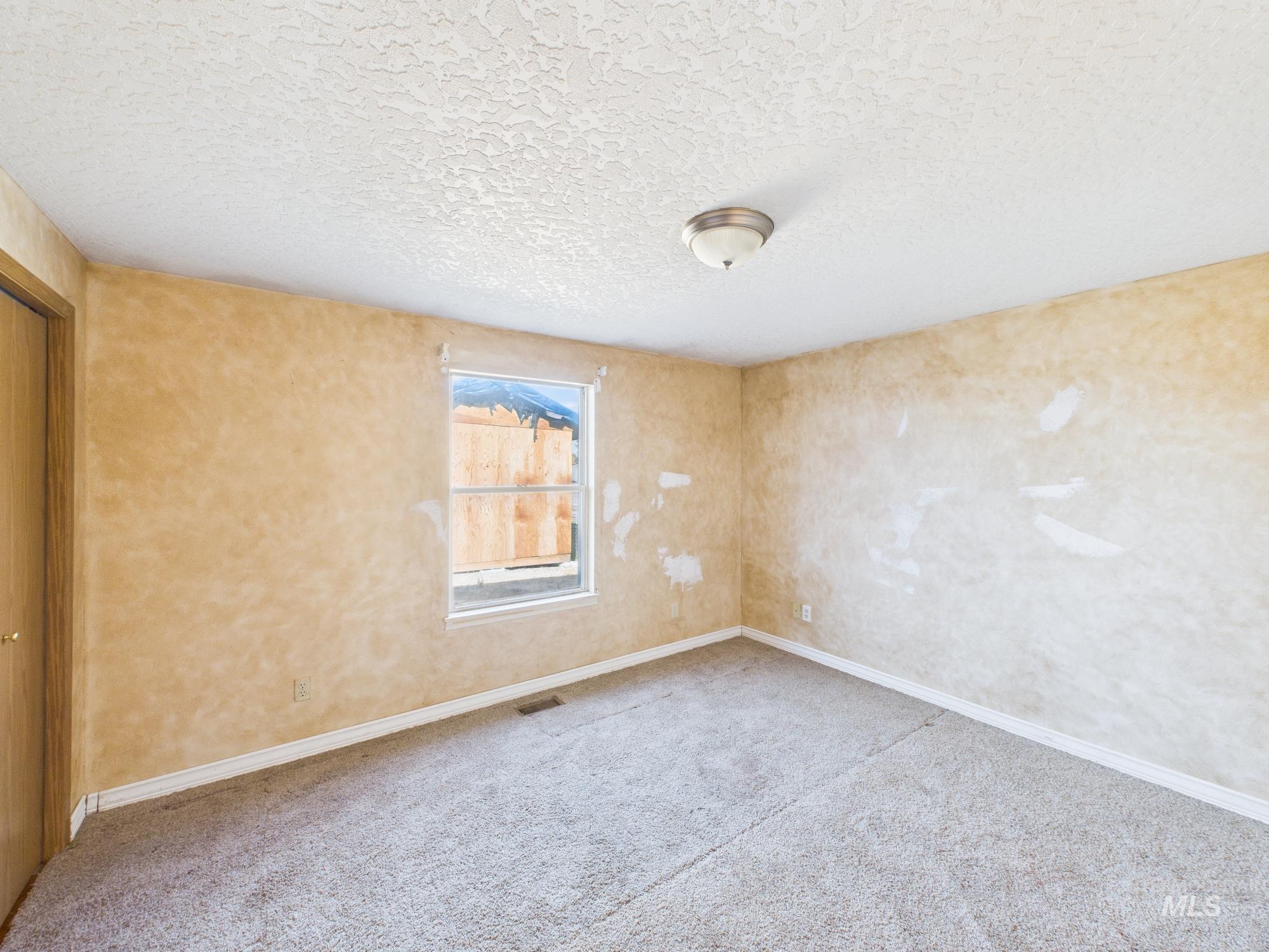 Carpeted spare room with a textured ceiling and baseboards