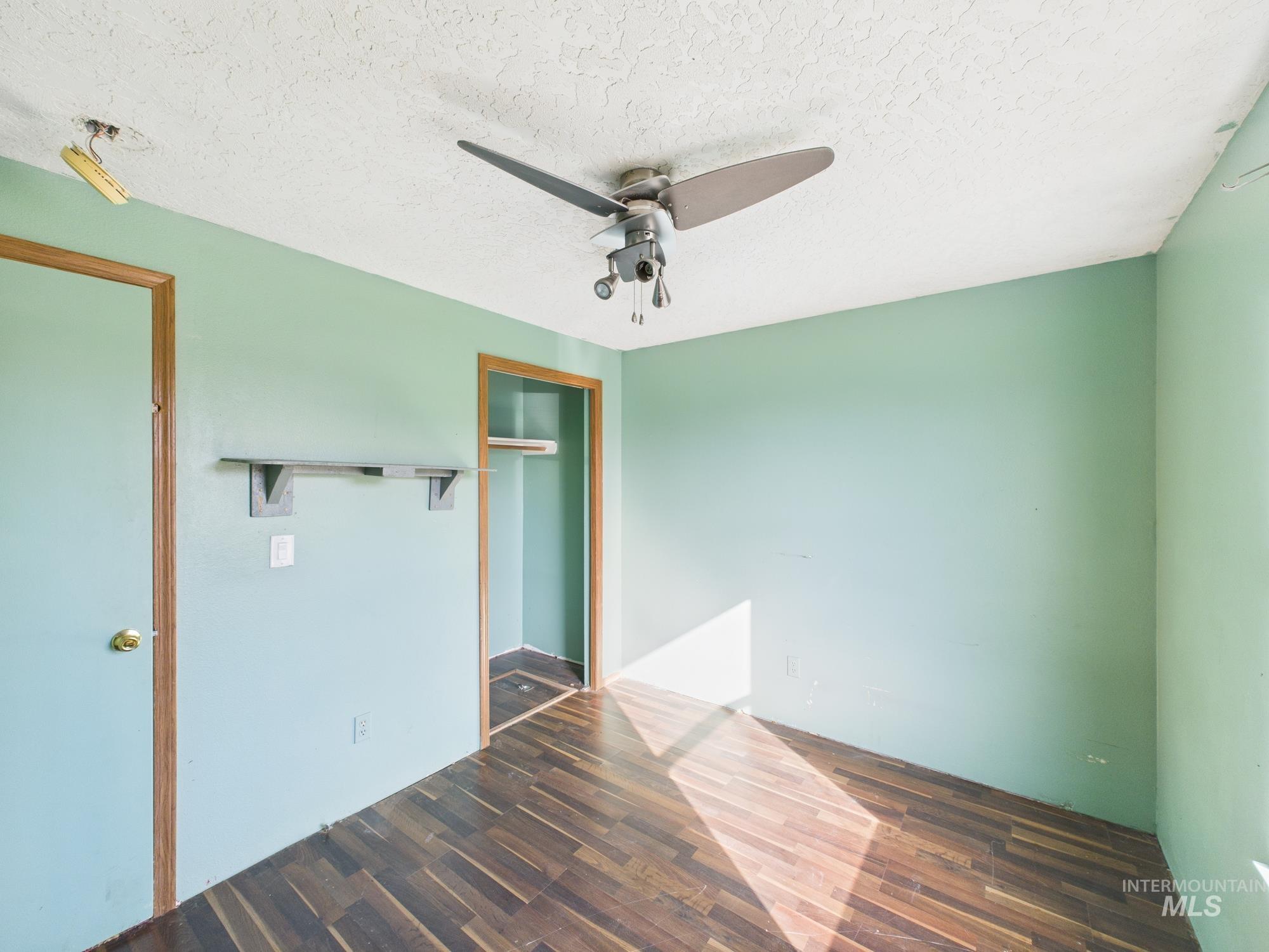 Unfurnished bedroom featuring dark wood-style floors, a textured ceiling, a closet, and a ceiling fan