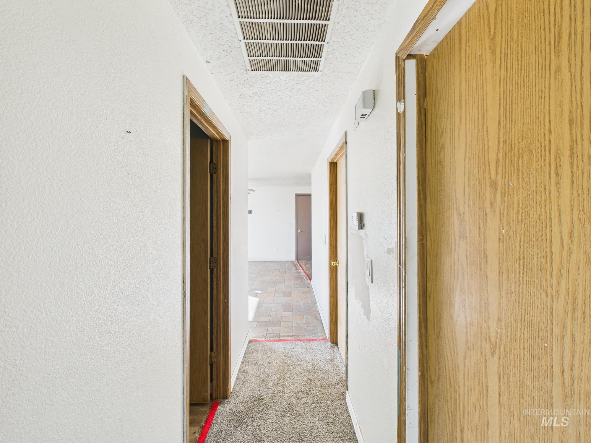 Corridor featuring light colored carpet, a textured ceiling, and light stone finish flooring
