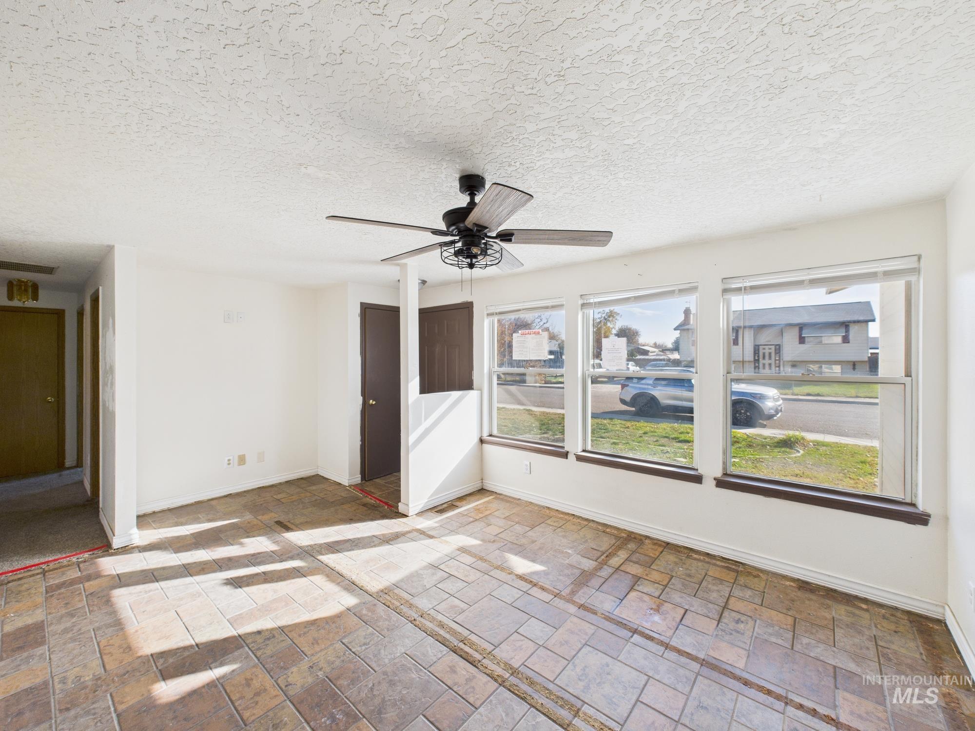 Empty room with stone tile flooring, ceiling fan, and a textured ceiling