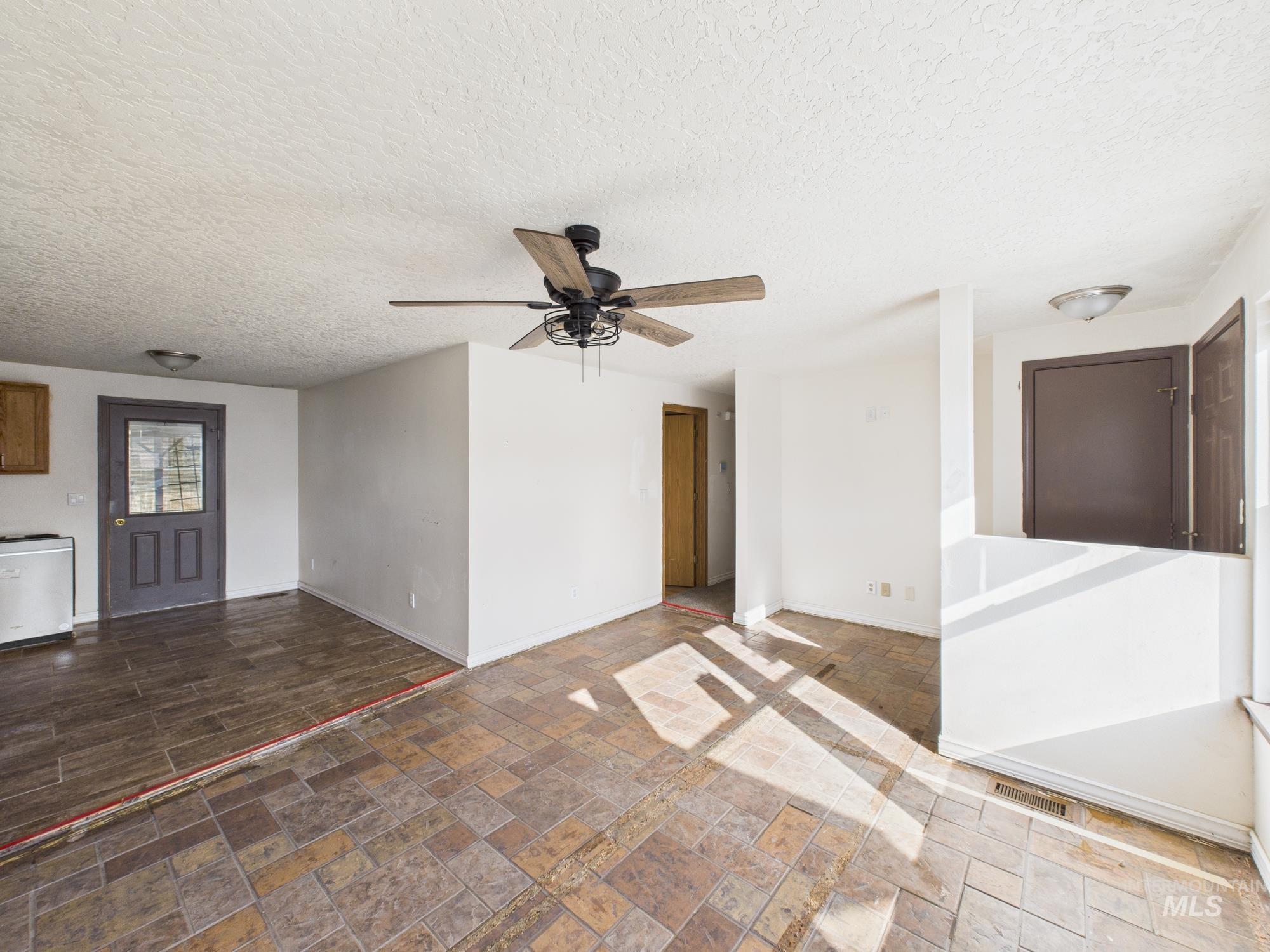 Unfurnished living room with a textured ceiling, stone tile floors, and a ceiling fan