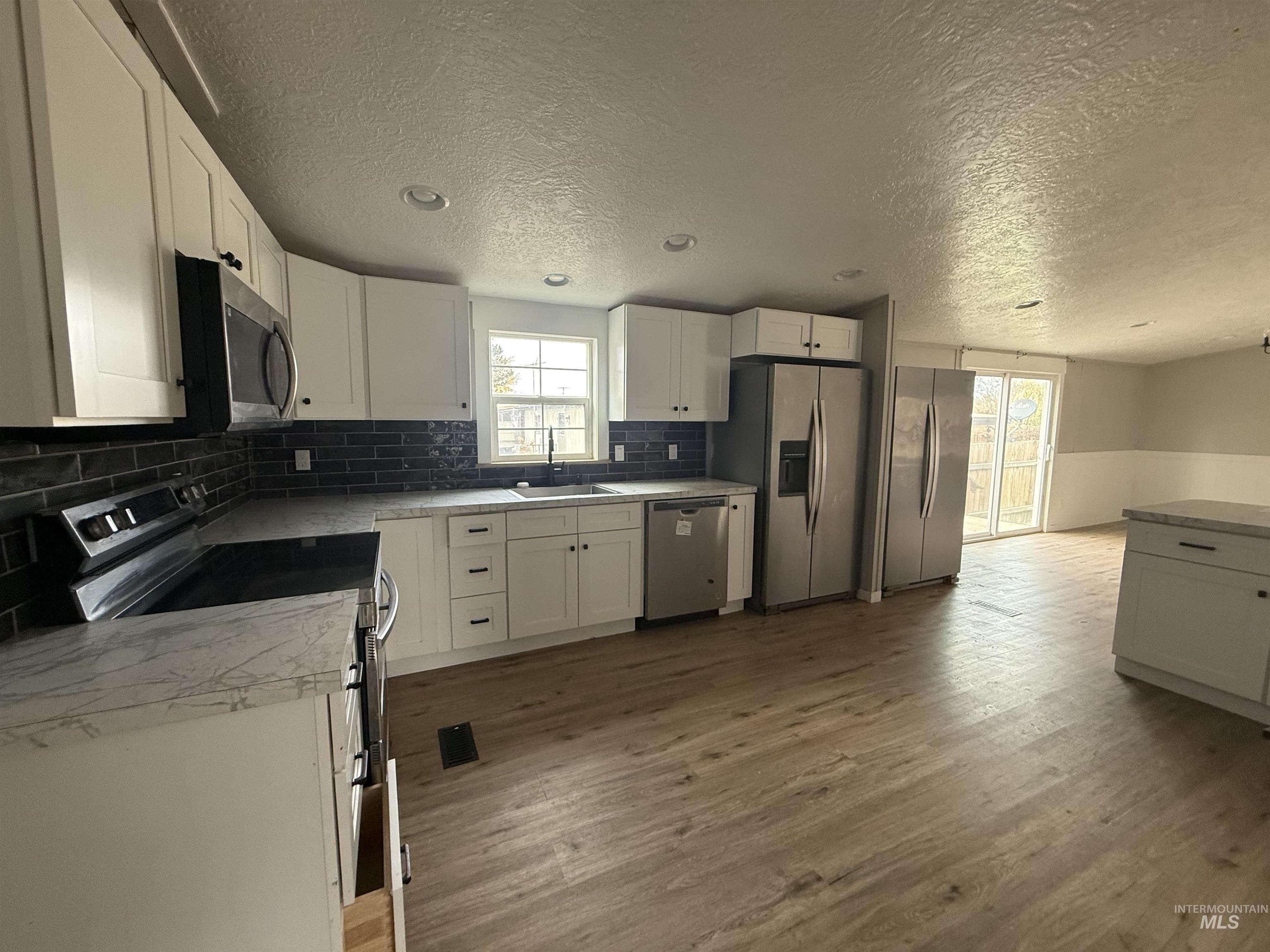 Kitchen featuring stainless steel appliances, white cabinets, dark wood-style floors, decorative backsplash, and a textured ceiling