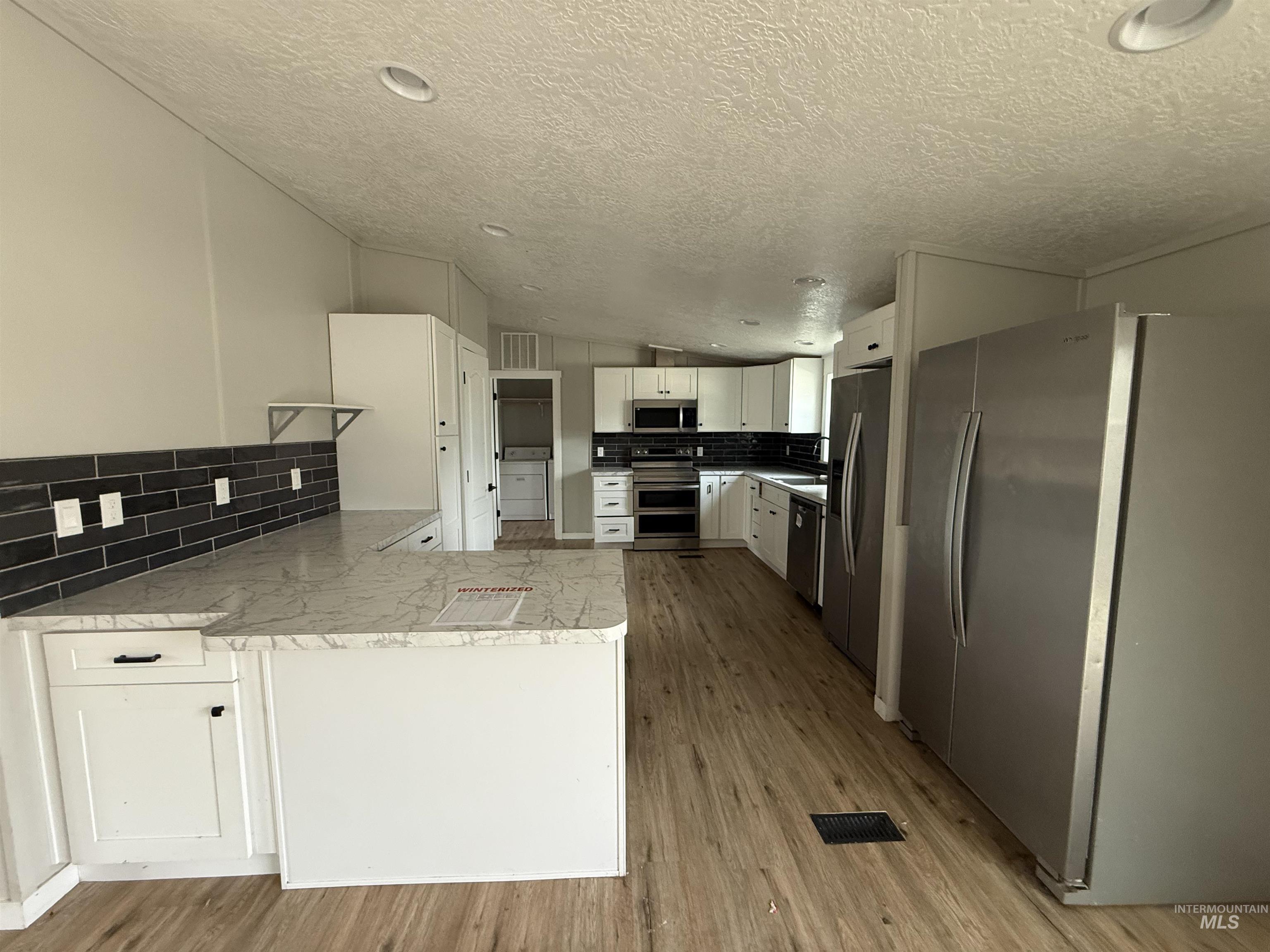 Kitchen with decorative backsplash, stainless steel appliances, white cabinetry, vaulted ceiling, and light wood-type flooring