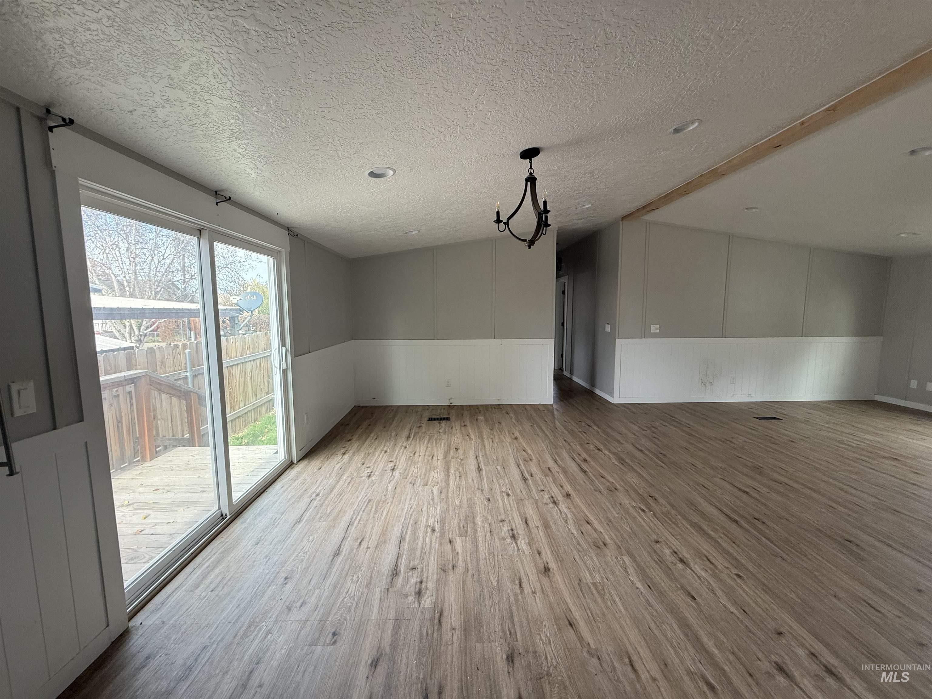 Unfurnished room with light wood-type flooring, a wainscoted wall, and a textured ceiling