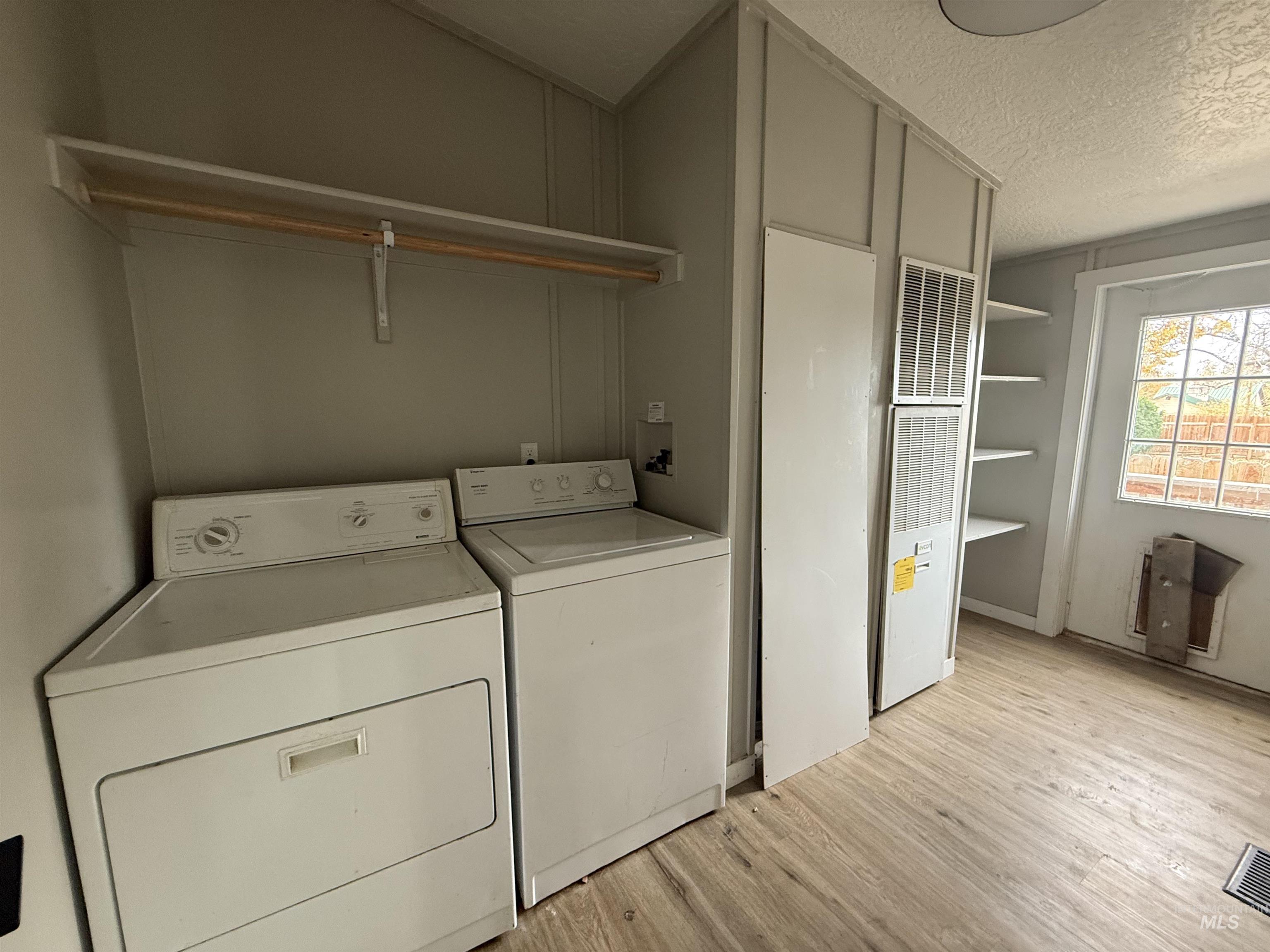 Washroom with light wood finished floors, a heating unit, washing machine and clothes dryer, and a textured ceiling
