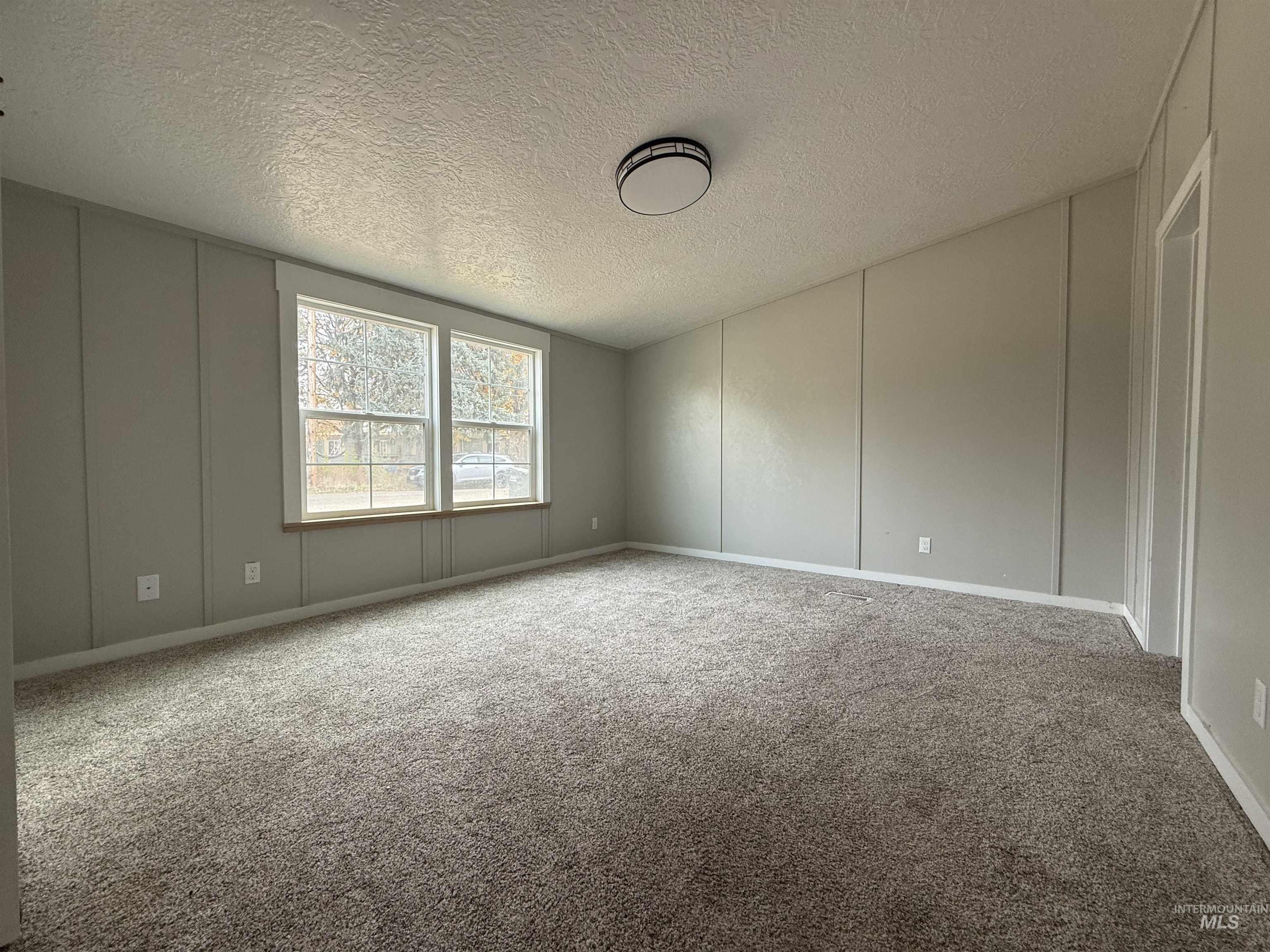 Unfurnished room featuring a decorative wall, light colored carpet, and a textured ceiling