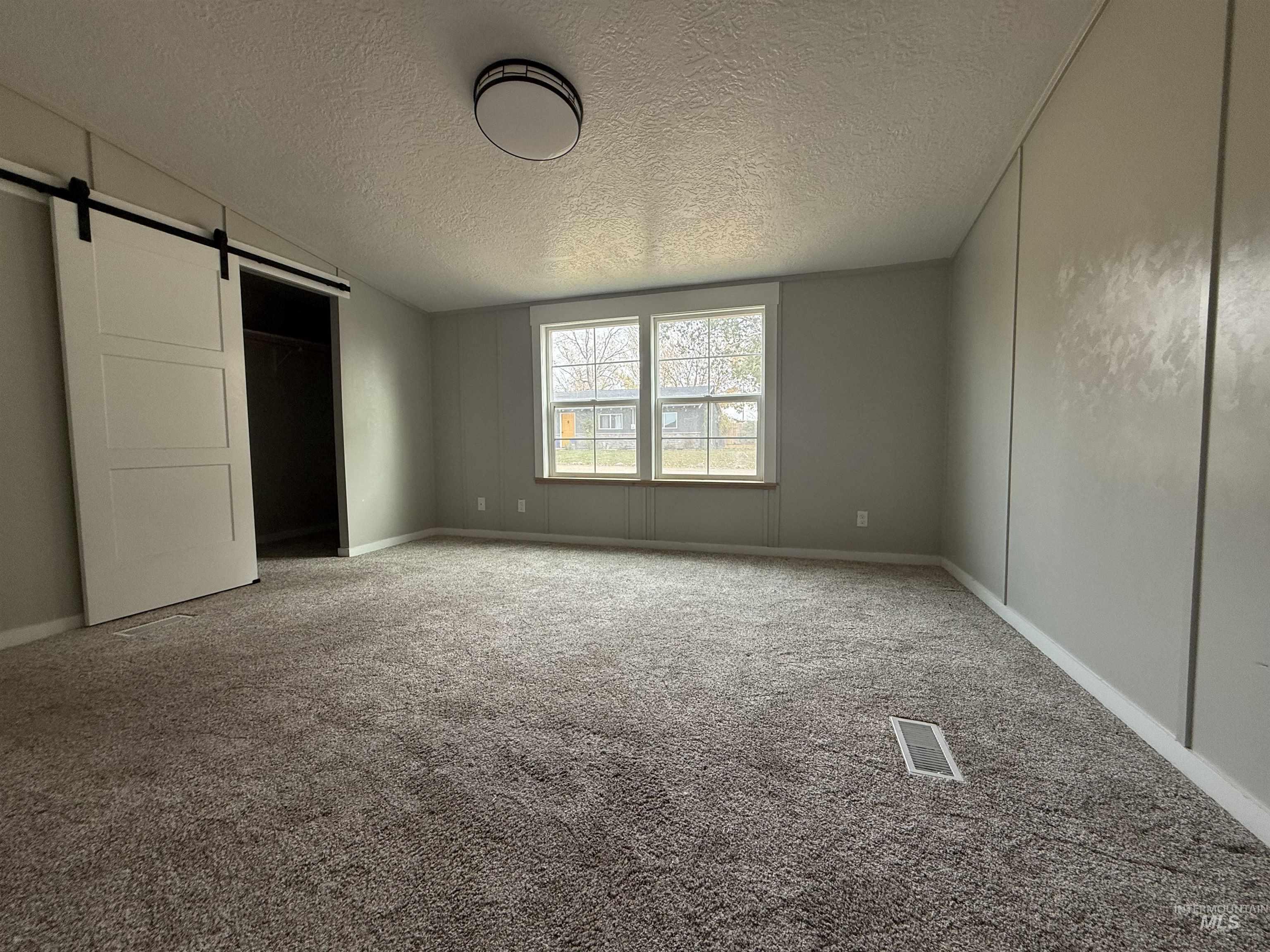 Unfurnished bedroom with a barn door, carpet, a textured ceiling, a closet, and lofted ceiling