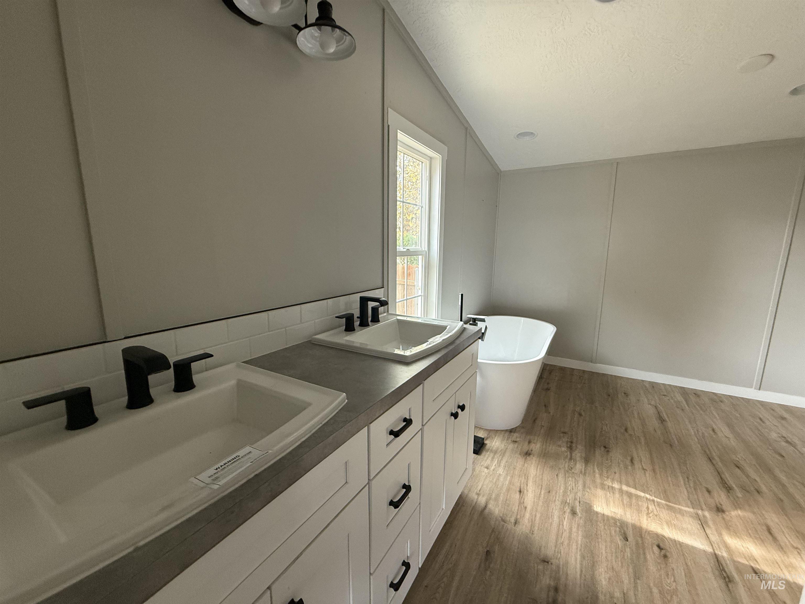 Full bathroom featuring a freestanding bath, light wood finished floors, double vanity, and a textured ceiling