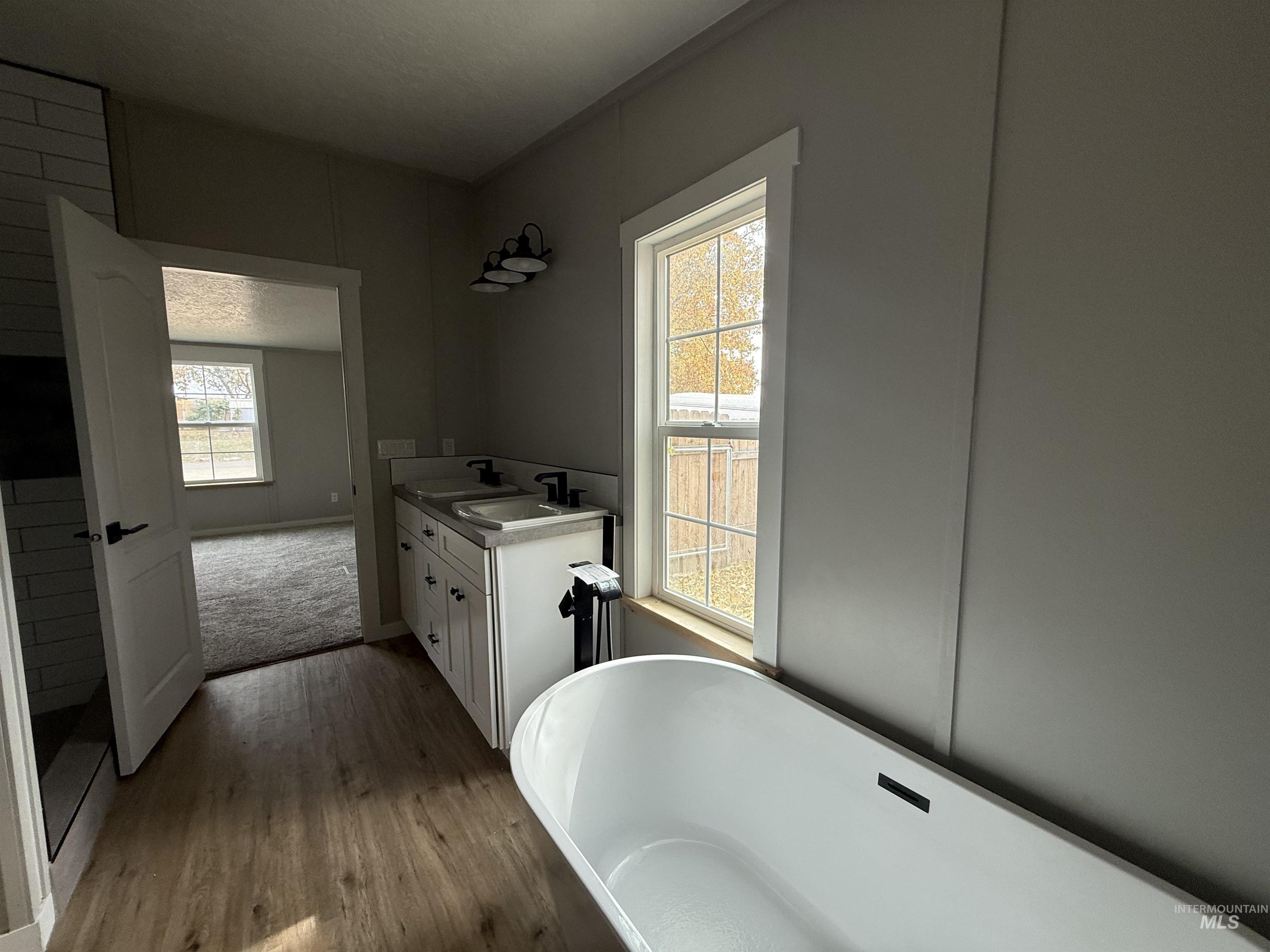 Bathroom featuring double vanity, a soaking tub, wood finished floors, and plenty of natural light
