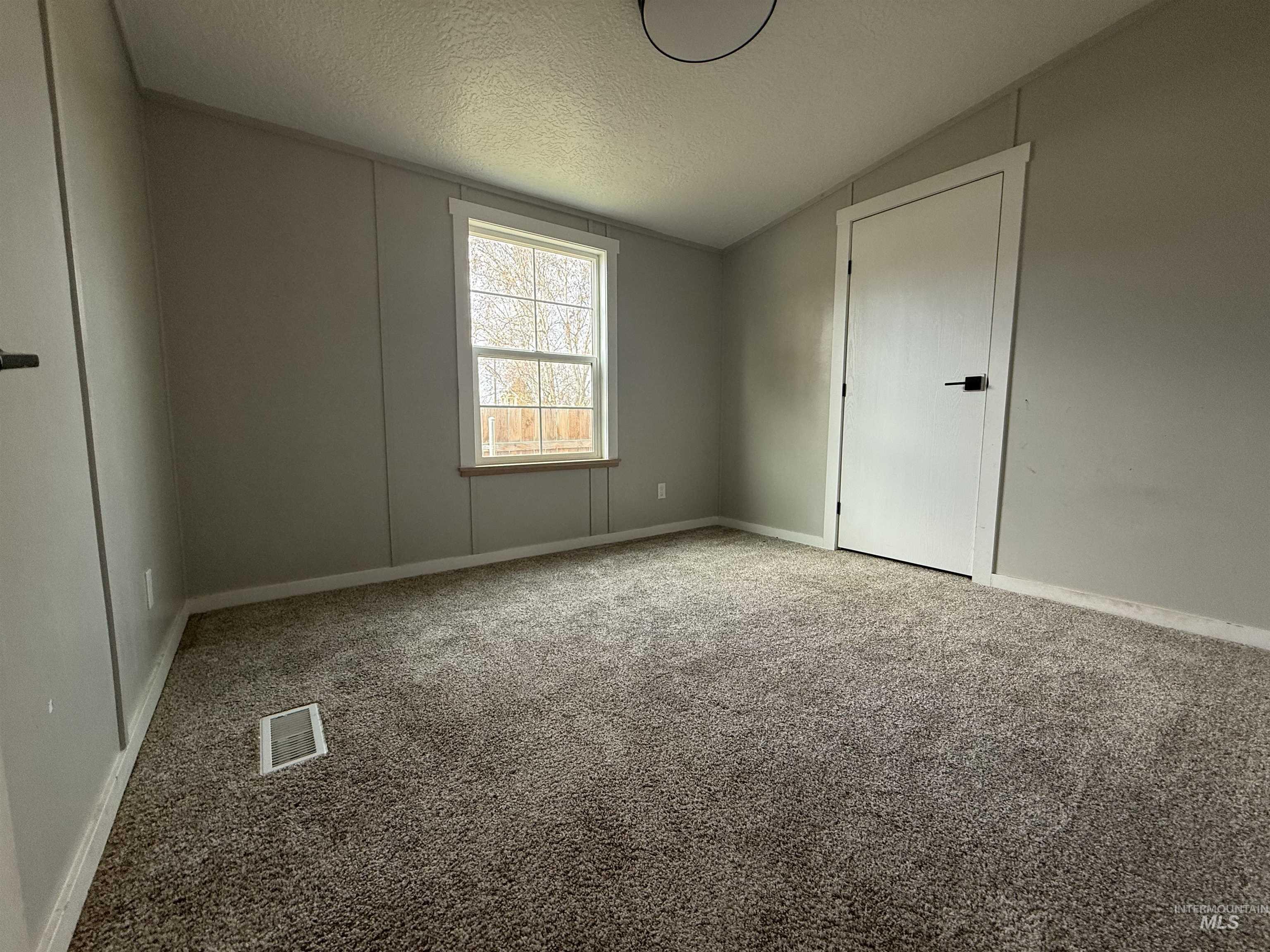 Unfurnished bedroom with light carpet, a textured ceiling, and vaulted ceiling