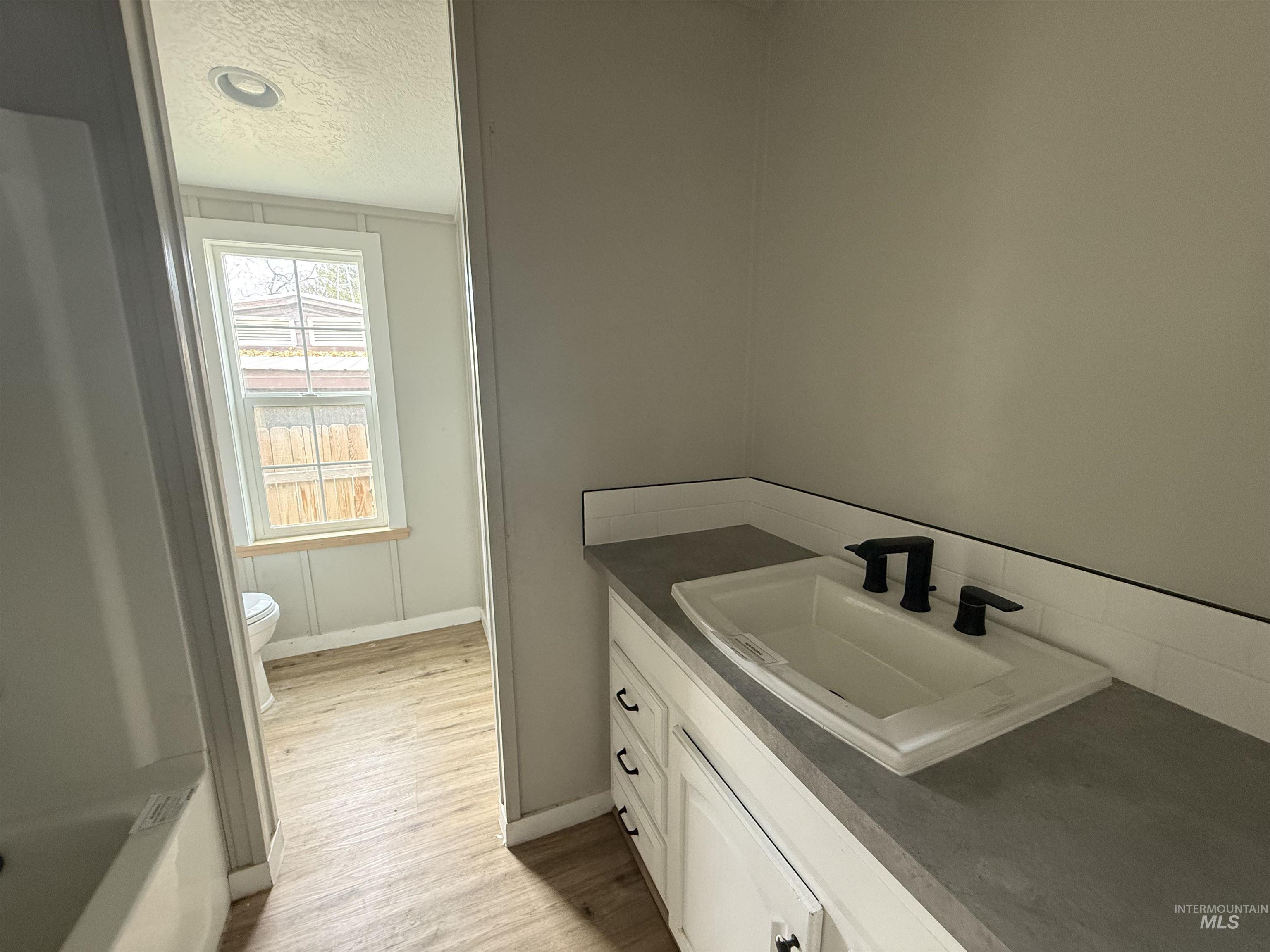 Full bath featuring a textured ceiling, vanity, and light wood finished floors