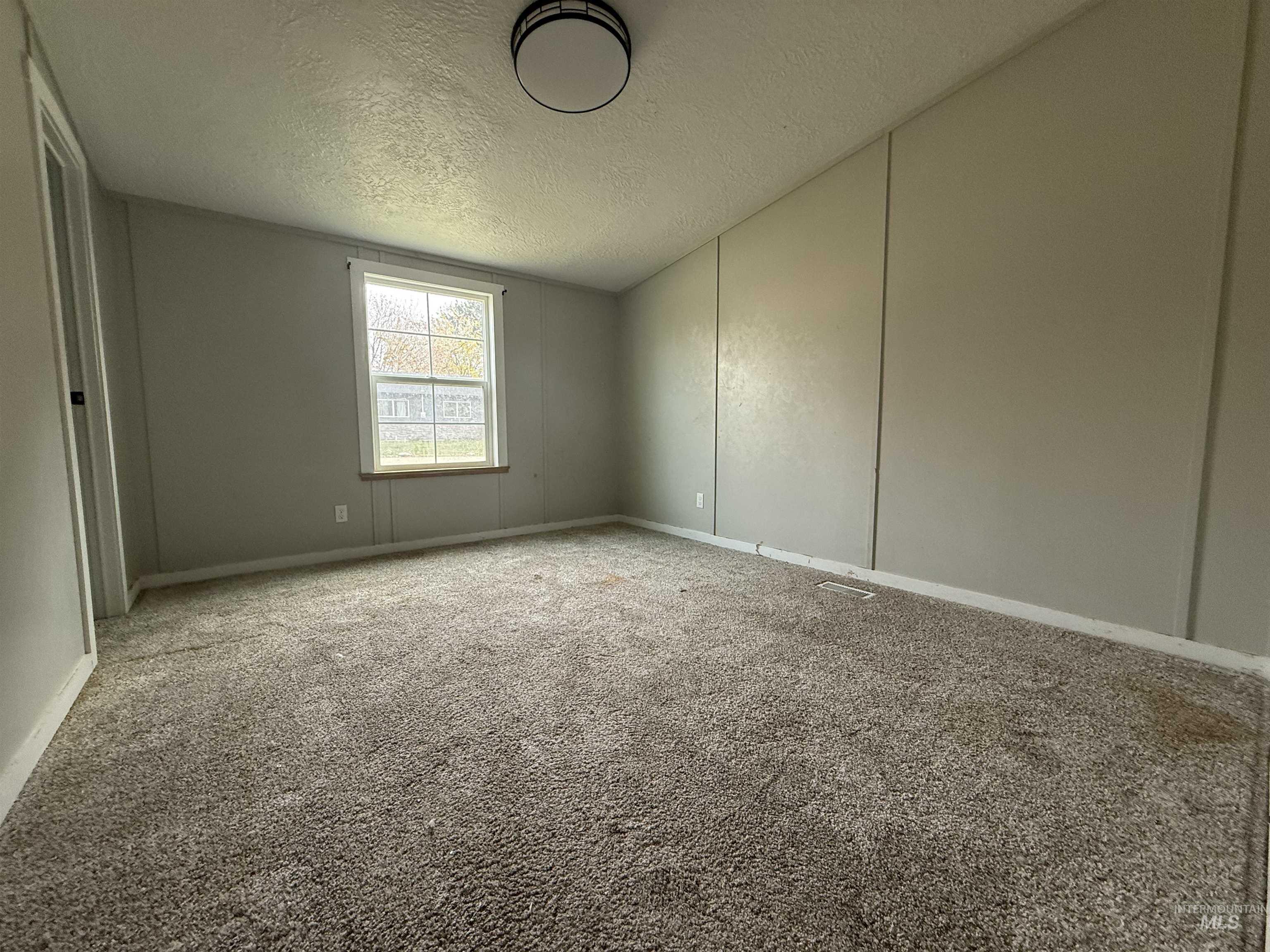 Carpeted spare room with a textured ceiling and baseboards
