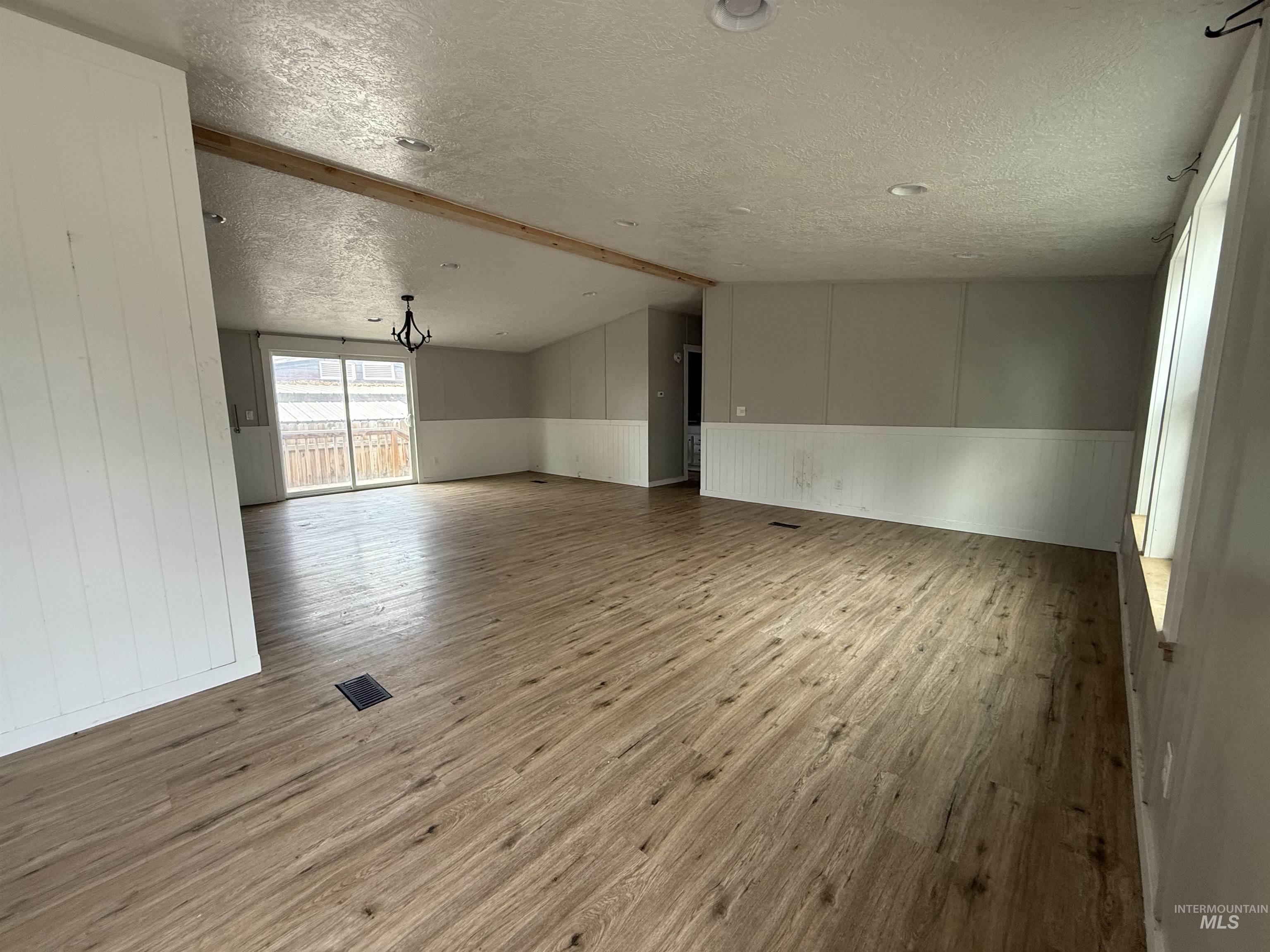 Unfurnished room with light wood-style flooring, a textured ceiling, a wainscoted wall, wood walls, and a chandelier