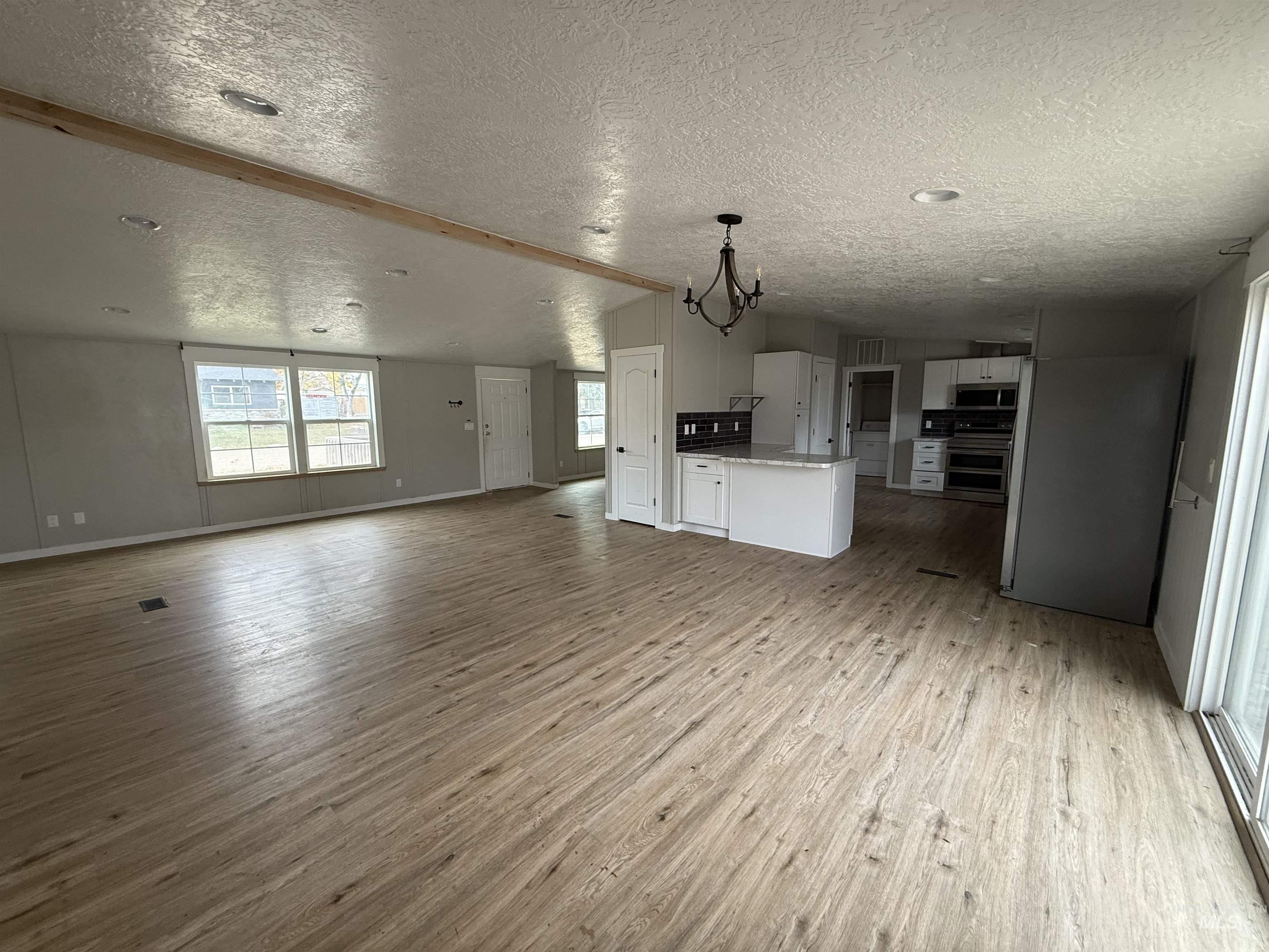 Unfurnished living room with a textured ceiling, light wood-style floors, and a chandelier