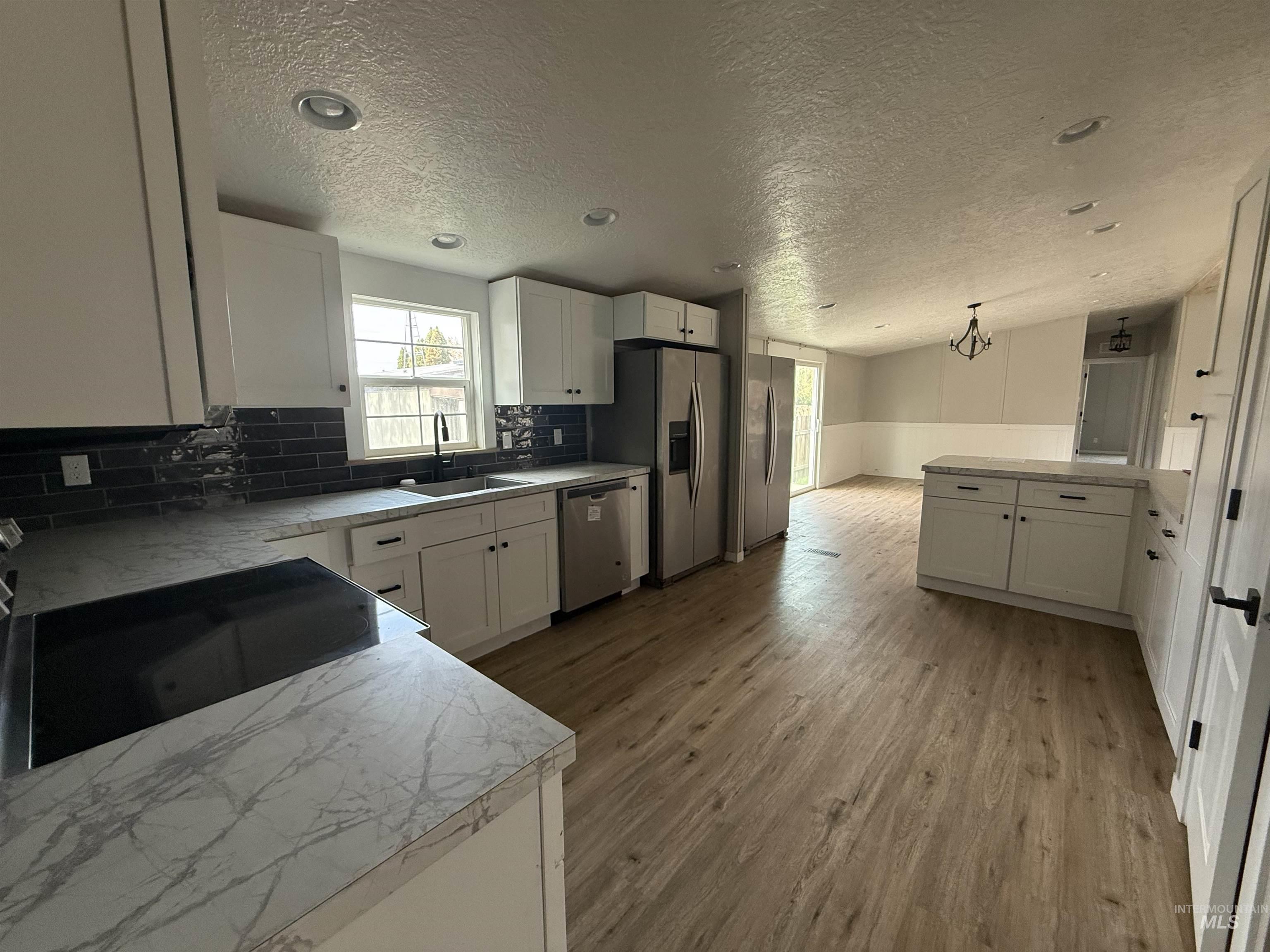 Kitchen featuring white cabinets, light countertops, light wood-type flooring, a peninsula, and wainscoting