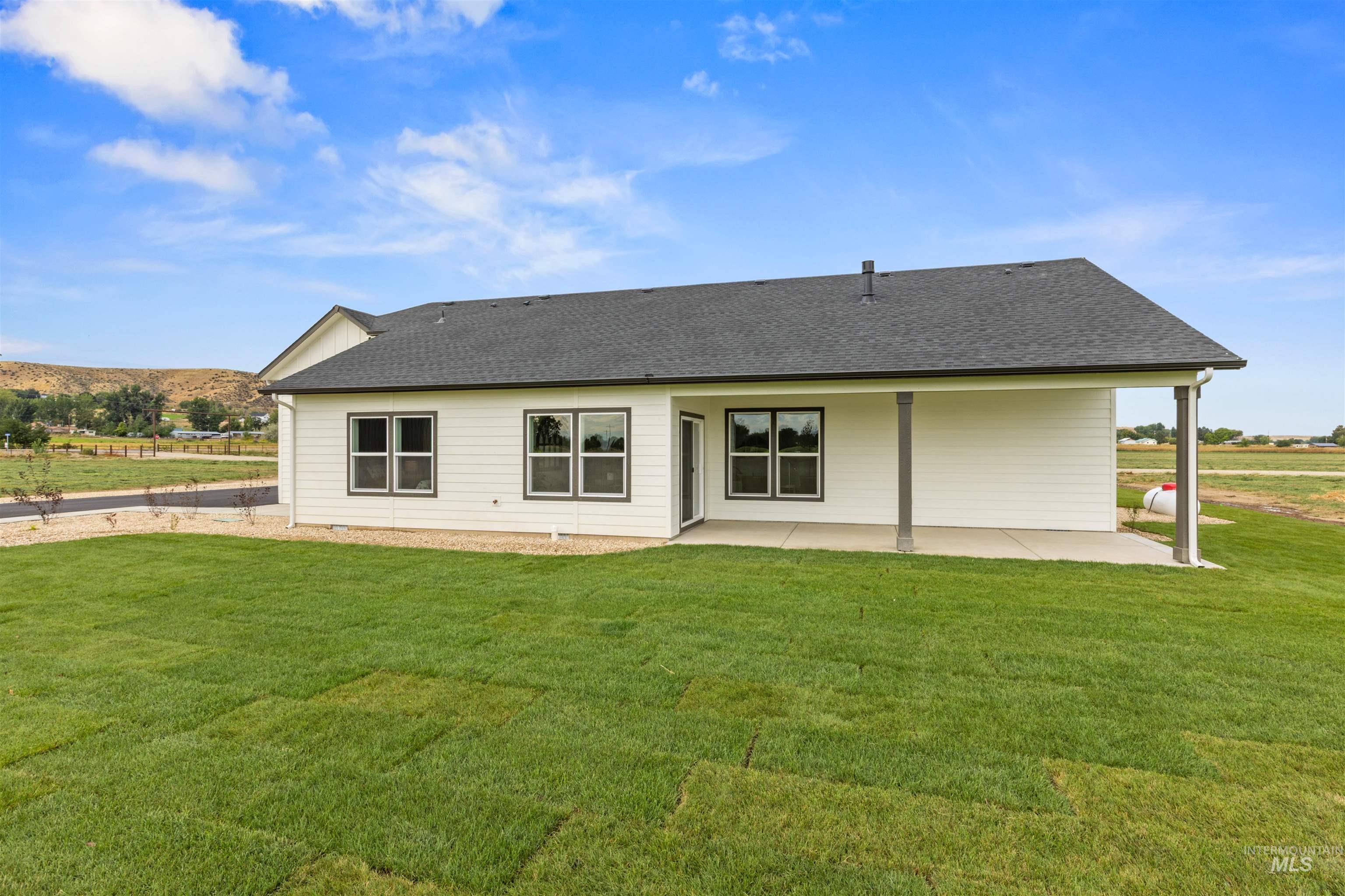 Back of house featuring a shingled roof, a patio area, and a yard