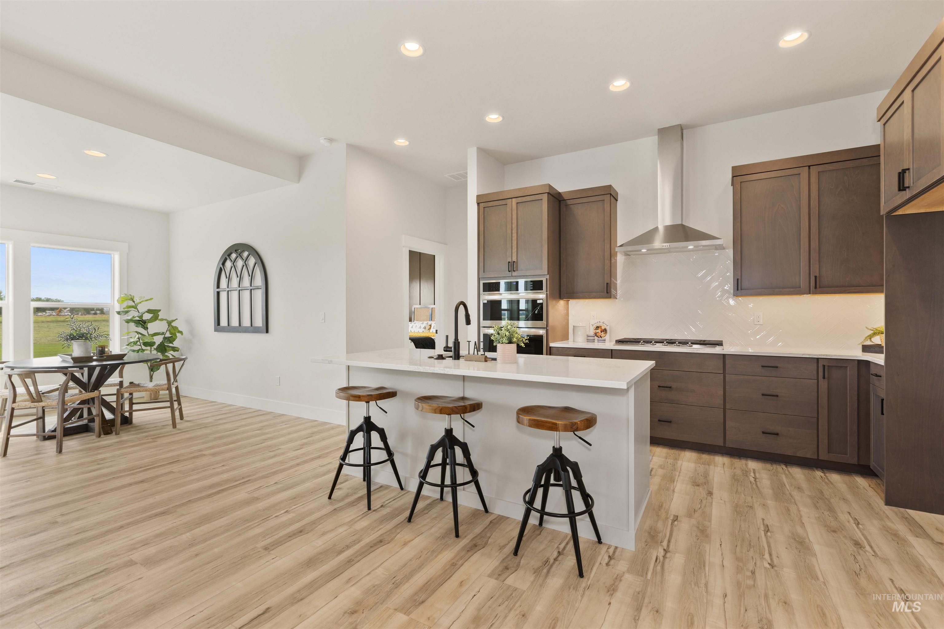 Kitchen featuring recessed lighting, a kitchen breakfast bar, light wood-type flooring, backsplash, and wall chimney exhaust hood