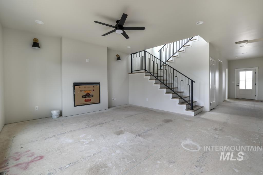 Unfurnished living room featuring stairway and ceiling fan