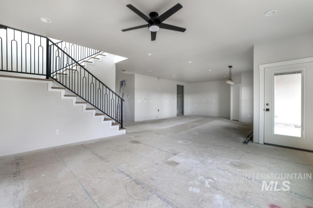 Unfurnished living room featuring ceiling fan and stairs