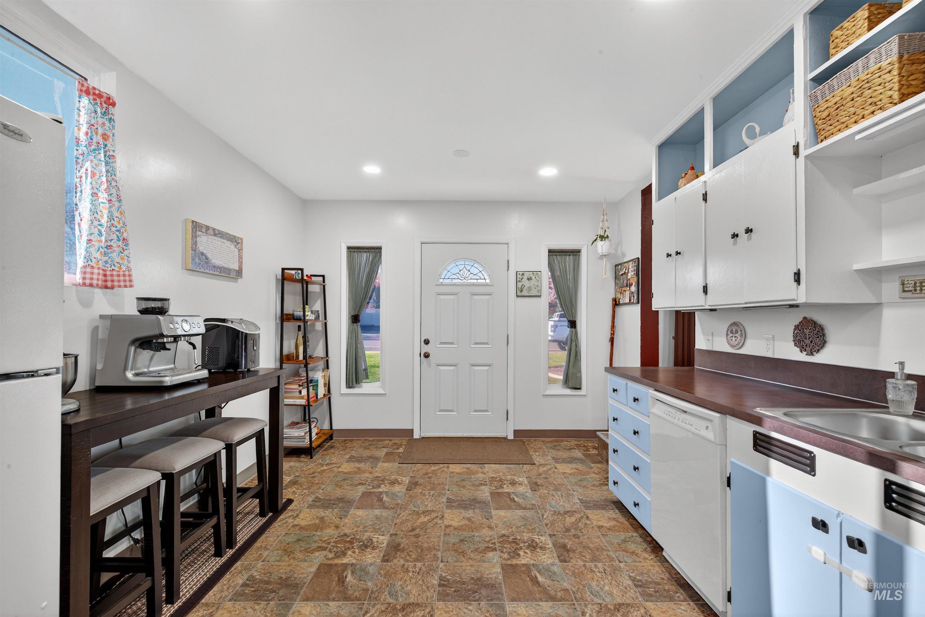Kitchen with open shelves, white appliances, white cabinetry, dark countertops, and stone finish flooring