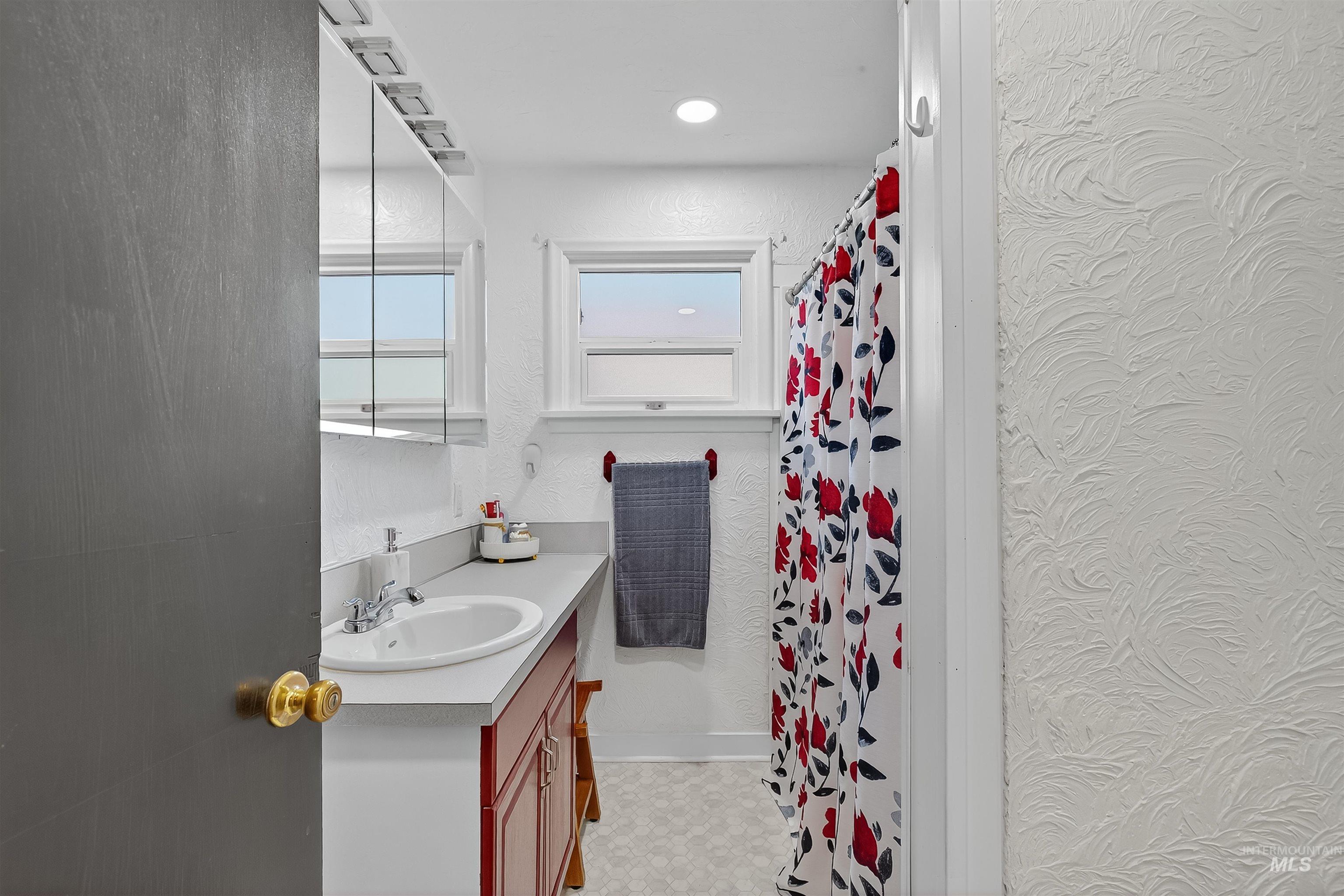 Full bath with vanity, a shower with shower curtain, a textured wall, and light flooring