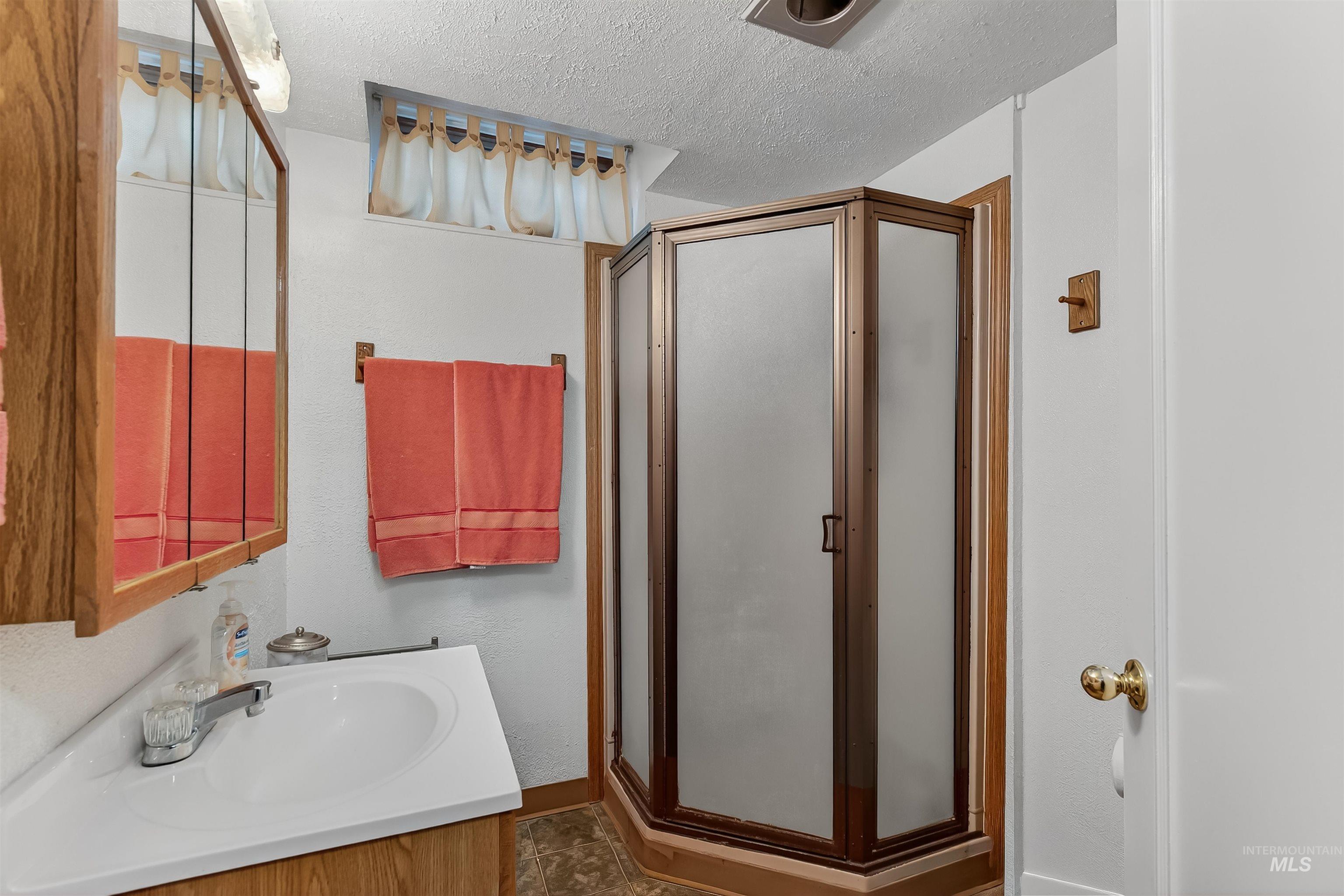 Full bathroom featuring a textured ceiling, vanity, and a stall shower