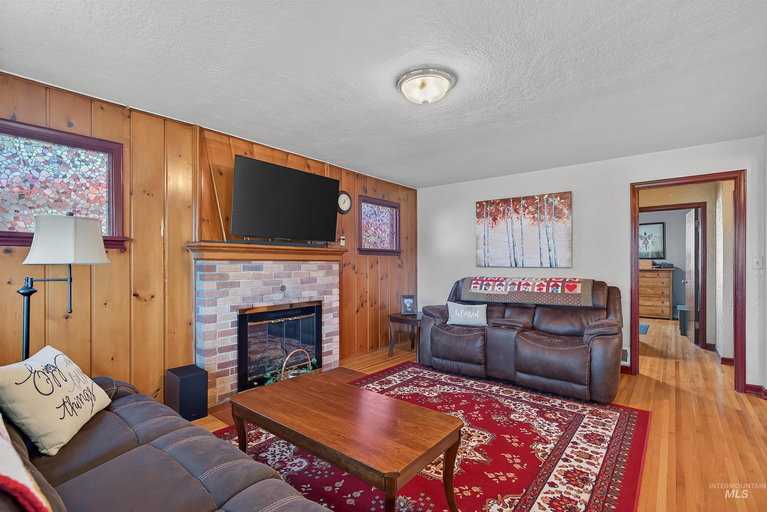 Living area with wood walls, a fireplace, light wood finished floors, a textured ceiling, and healthy amount of natural light
