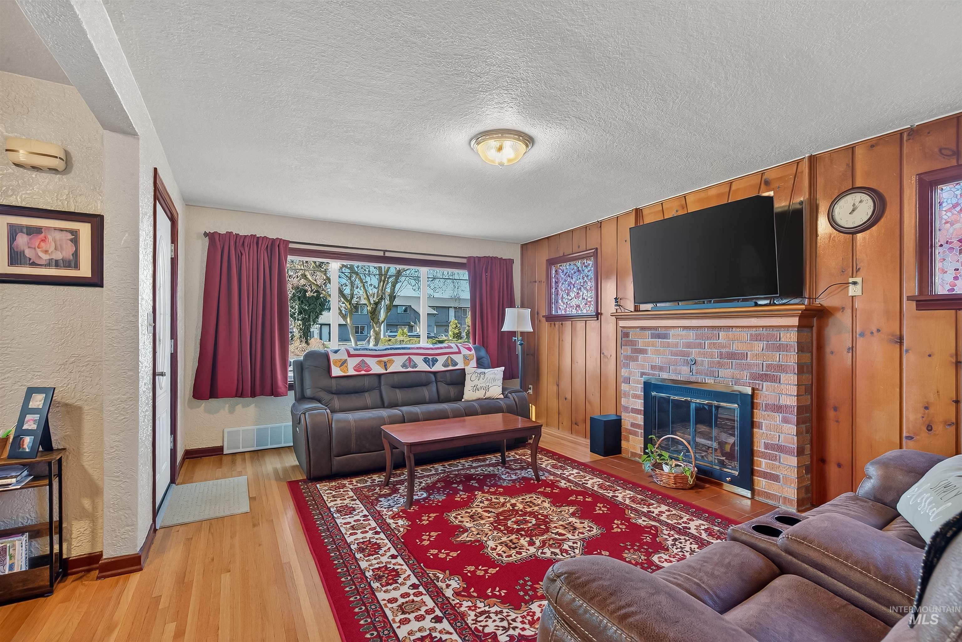 Living area featuring light wood-style flooring, a textured ceiling, a brick fireplace, and a textured wall