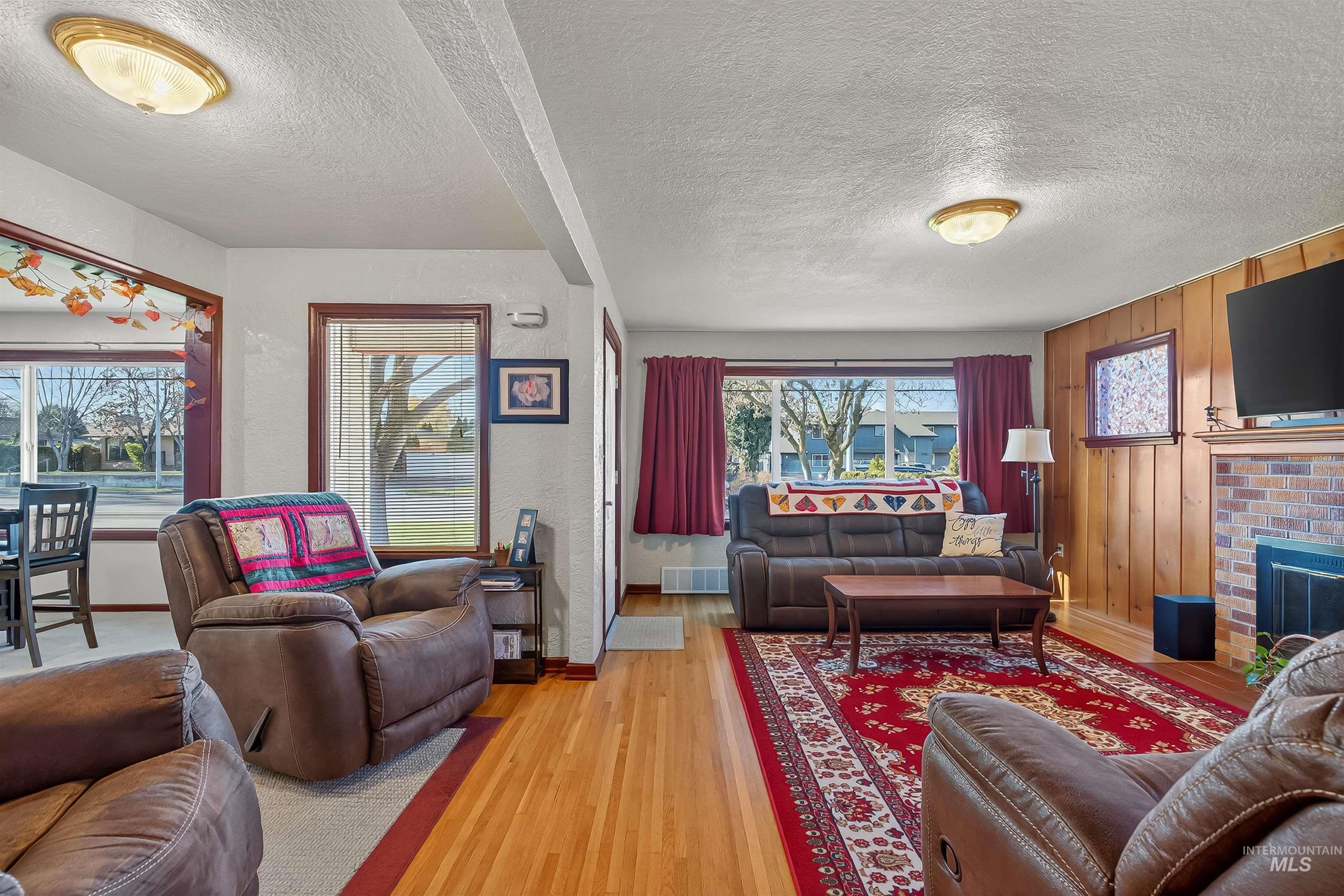 Living area with a textured ceiling, wood finished floors, a fireplace, a textured wall, and wood walls
