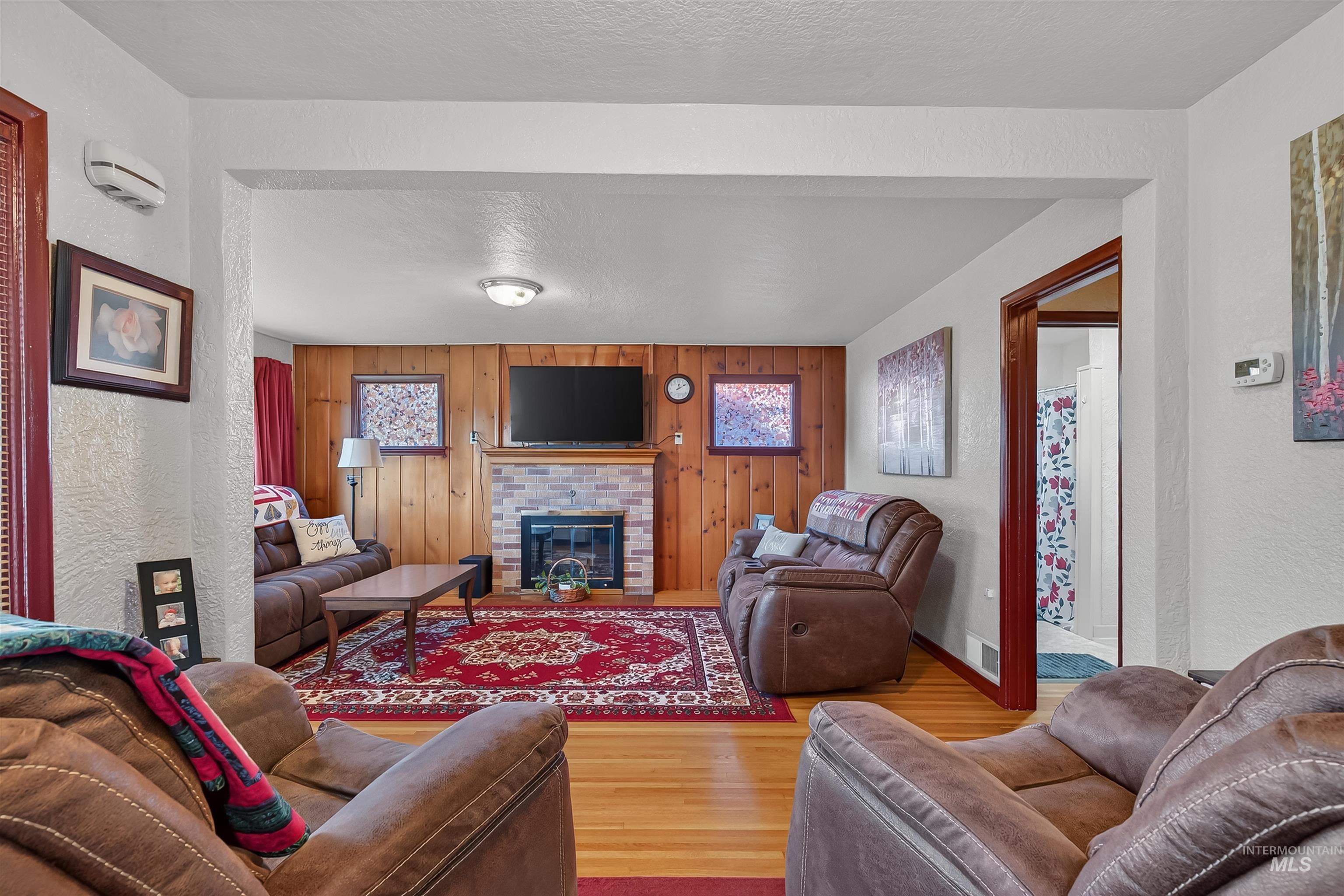 Living room featuring a textured wall, wood finished floors, wooden walls, a textured ceiling, and a brick fireplace