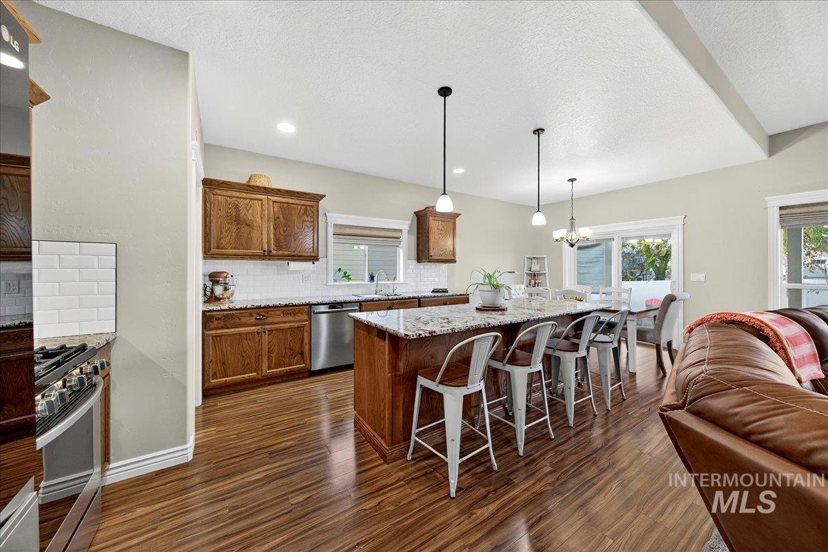 Kitchen with decorative backsplash, brown cabinetry, light stone counters, a kitchen island, and a breakfast bar area