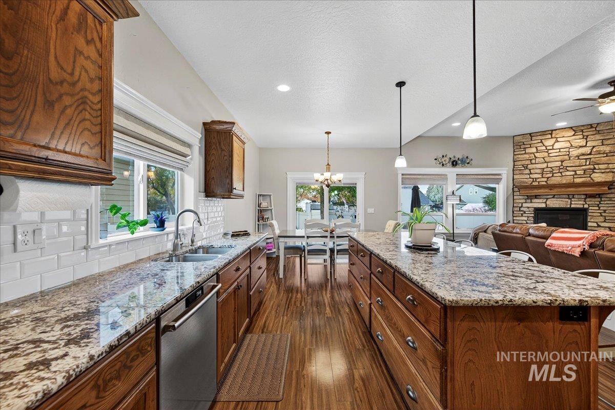 Kitchen with light stone counters, dark wood finished floors, decorative light fixtures, dishwasher, and a textured ceiling