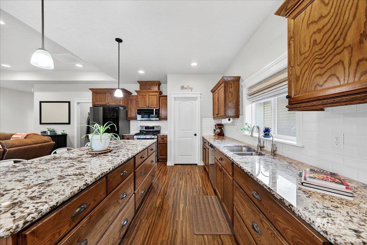 Kitchen featuring dark wood finished floors, pendant lighting, light stone counters, brown cabinetry, and stainless steel appliances