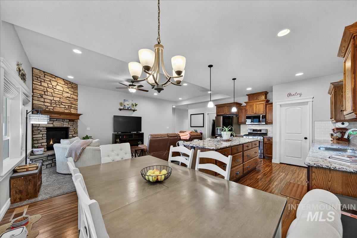 Dining room with a stone fireplace, dark wood finished floors, a chandelier, recessed lighting, and a ceiling fan