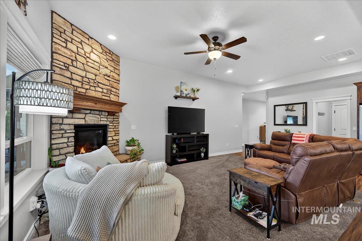 Living room with carpet, a stone fireplace, ceiling fan, recessed lighting, and a textured ceiling