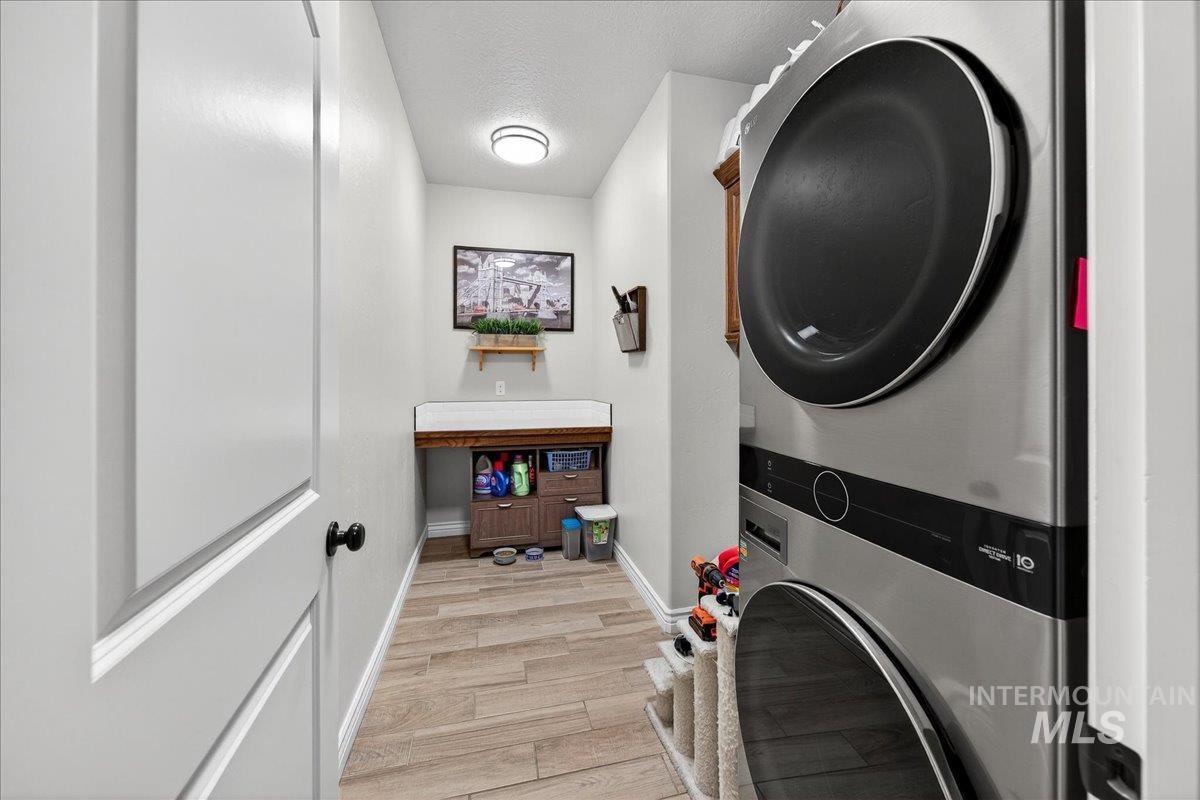 Laundry area with light wood-style flooring, stacked washer / dryer, and a textured ceiling