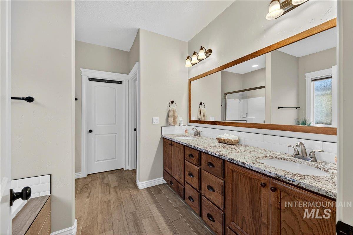 Bathroom with double vanity, light wood finished floors, and a stall shower