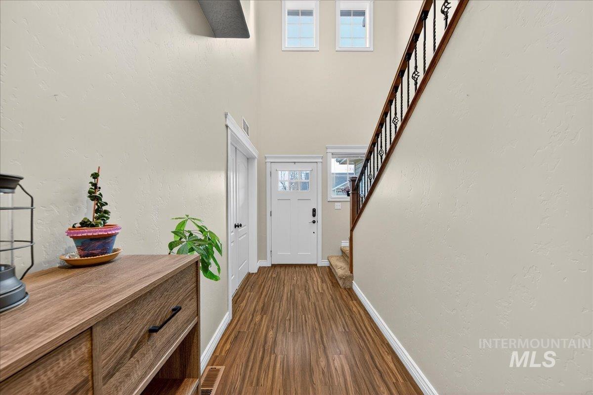 Doorway with a textured wall, stairway, wood finished floors, and a towering ceiling