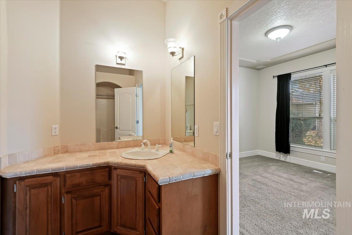 Full bath featuring a textured ceiling, light carpet, and vanity
