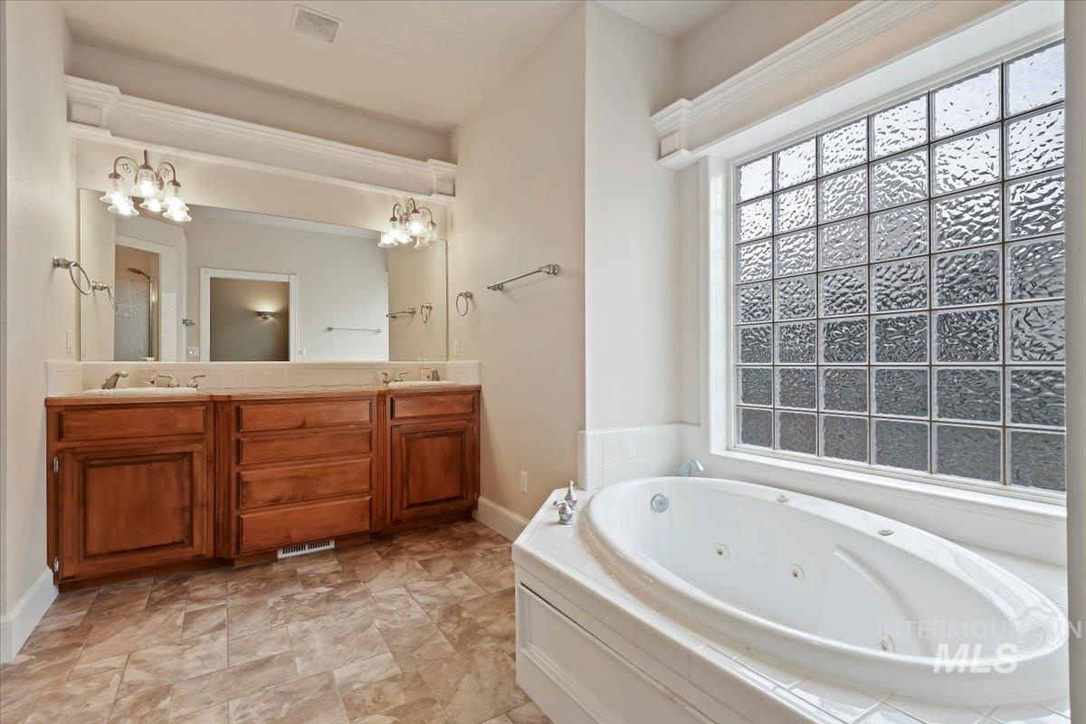 Full bath featuring a tub with jets, double vanity, and a chandelier