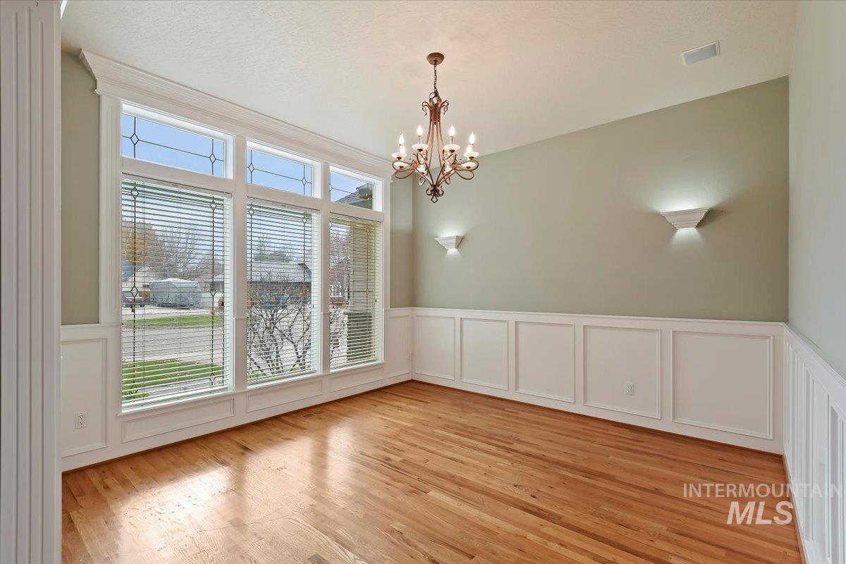 Unfurnished dining area featuring a decorative wall, light wood finished floors, a wainscoted wall, and a chandelier