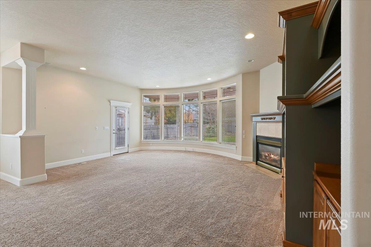 Unfurnished living room with a tile fireplace, light carpet, a textured ceiling, recessed lighting, and decorative columns