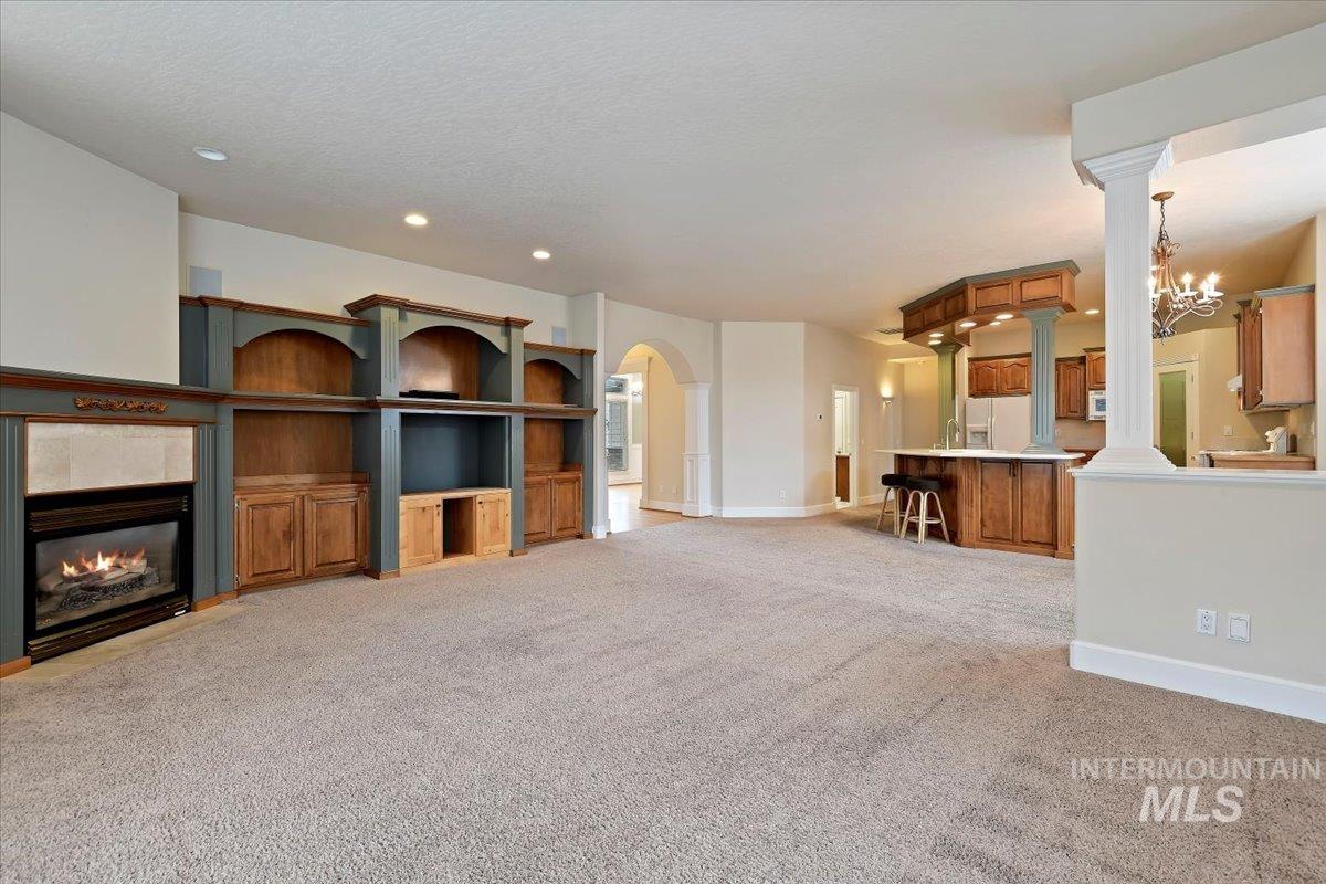 Unfurnished living room with light colored carpet, a tiled fireplace, a chandelier, recessed lighting, and decorative columns