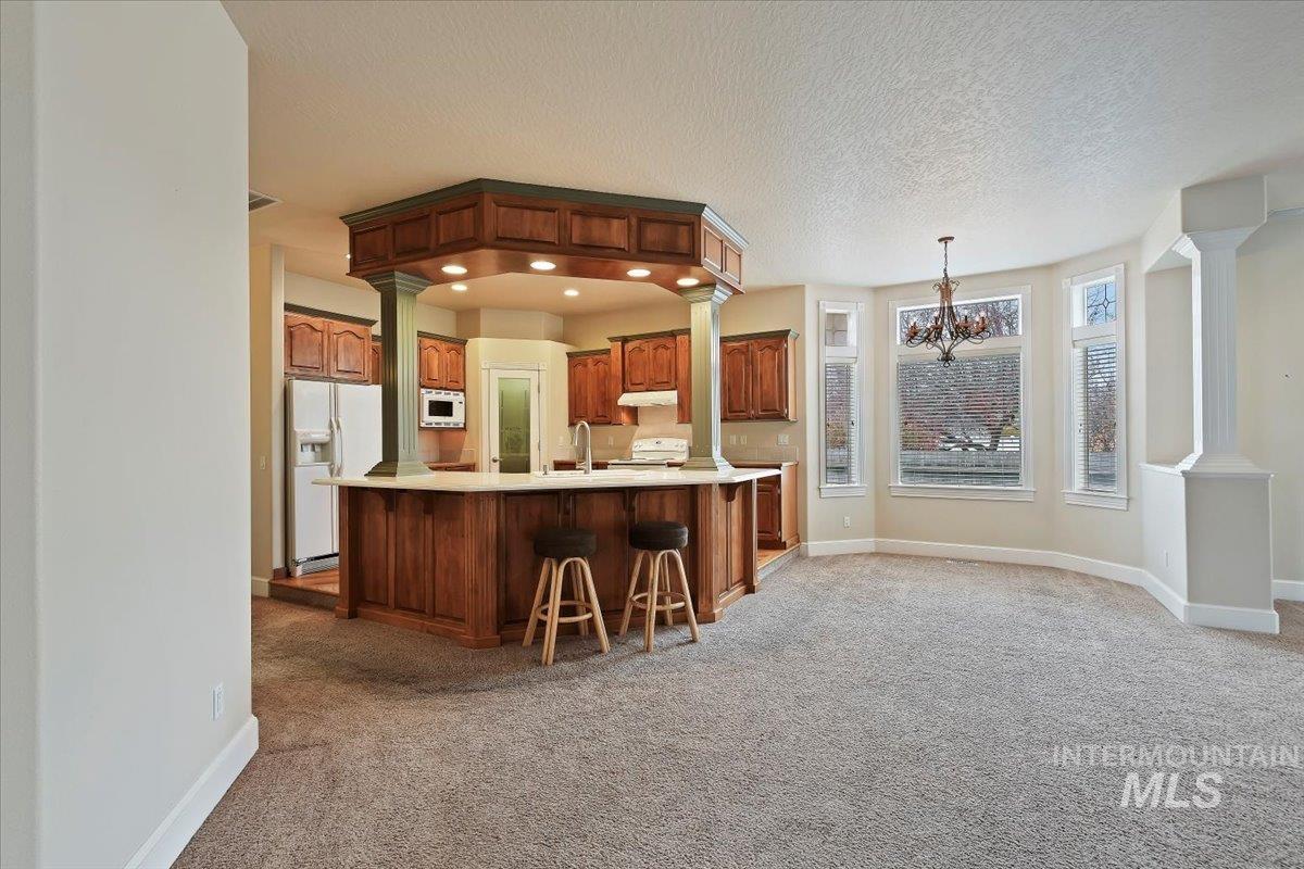 Kitchen with dark colored carpet, light countertops, a chandelier, white appliances, and pendant lighting