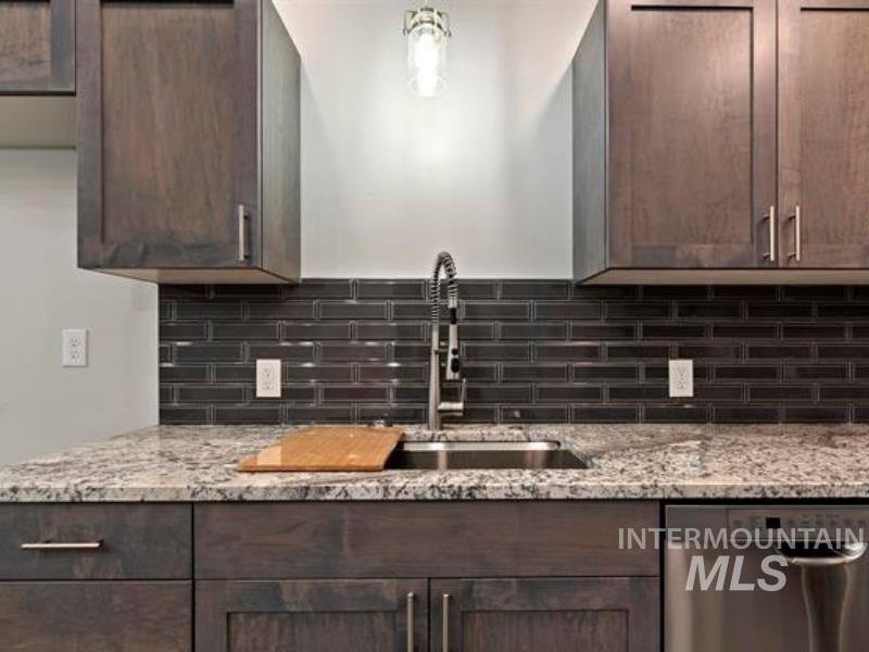 Kitchen with stainless steel dishwasher, tasteful backsplash, light stone counters, and dark brown cabinetry