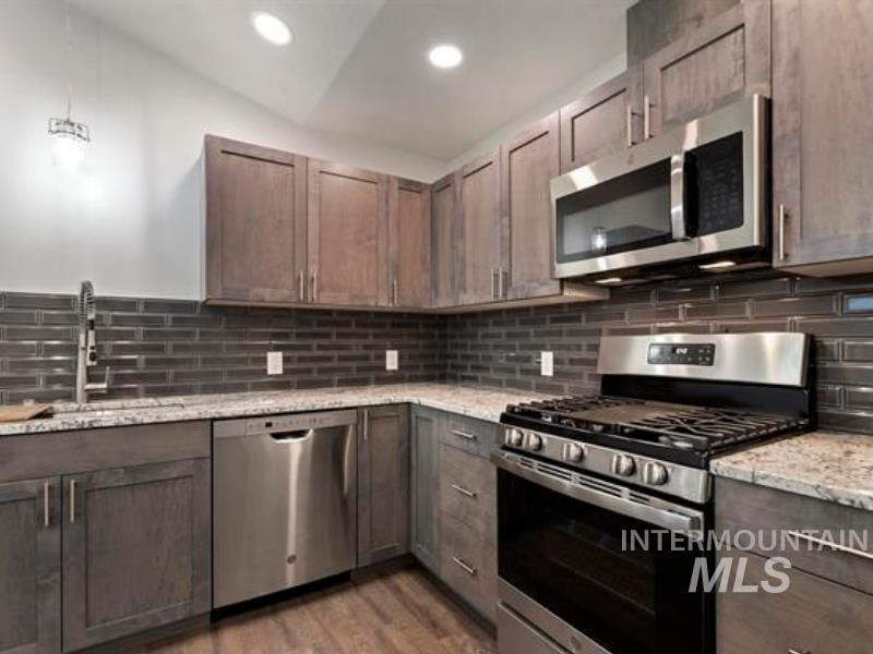 Kitchen with appliances with stainless steel finishes, light stone counters, backsplash, light wood-style floors, and recessed lighting