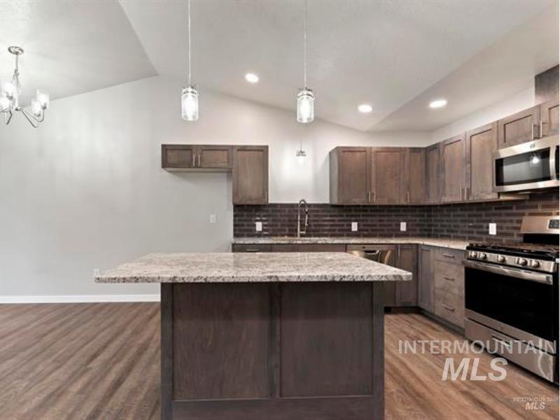 Kitchen with stainless steel appliances, decorative light fixtures, vaulted ceiling, tasteful backsplash, and dark wood-style flooring