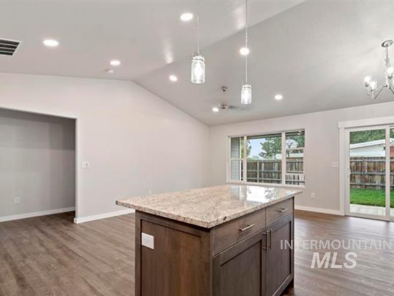 Kitchen with lofted ceiling, dark wood finished floors, light stone counters, pendant lighting, and open floor plan