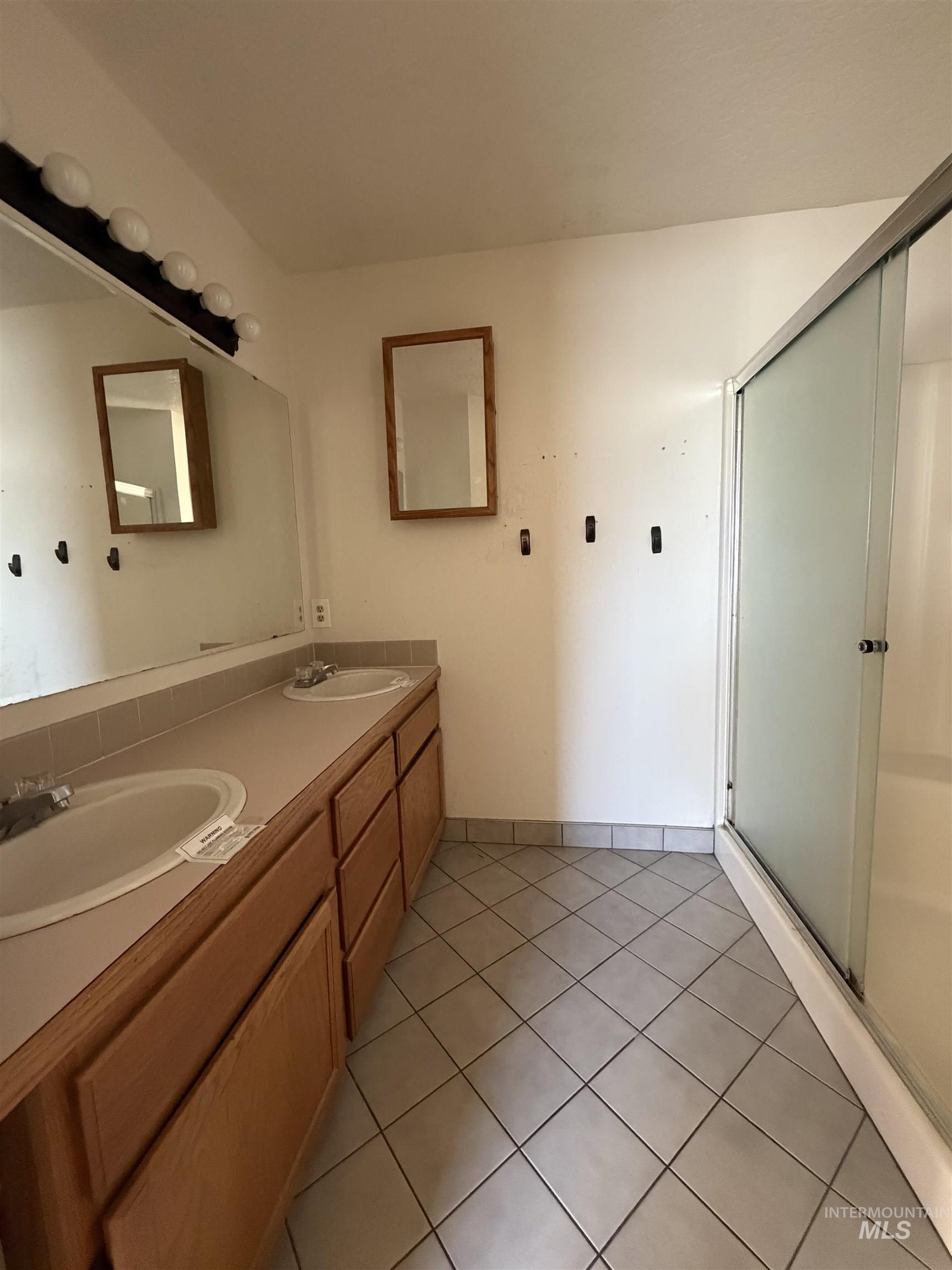 Full bath with light tile patterned floors, double vanity, and a stall shower