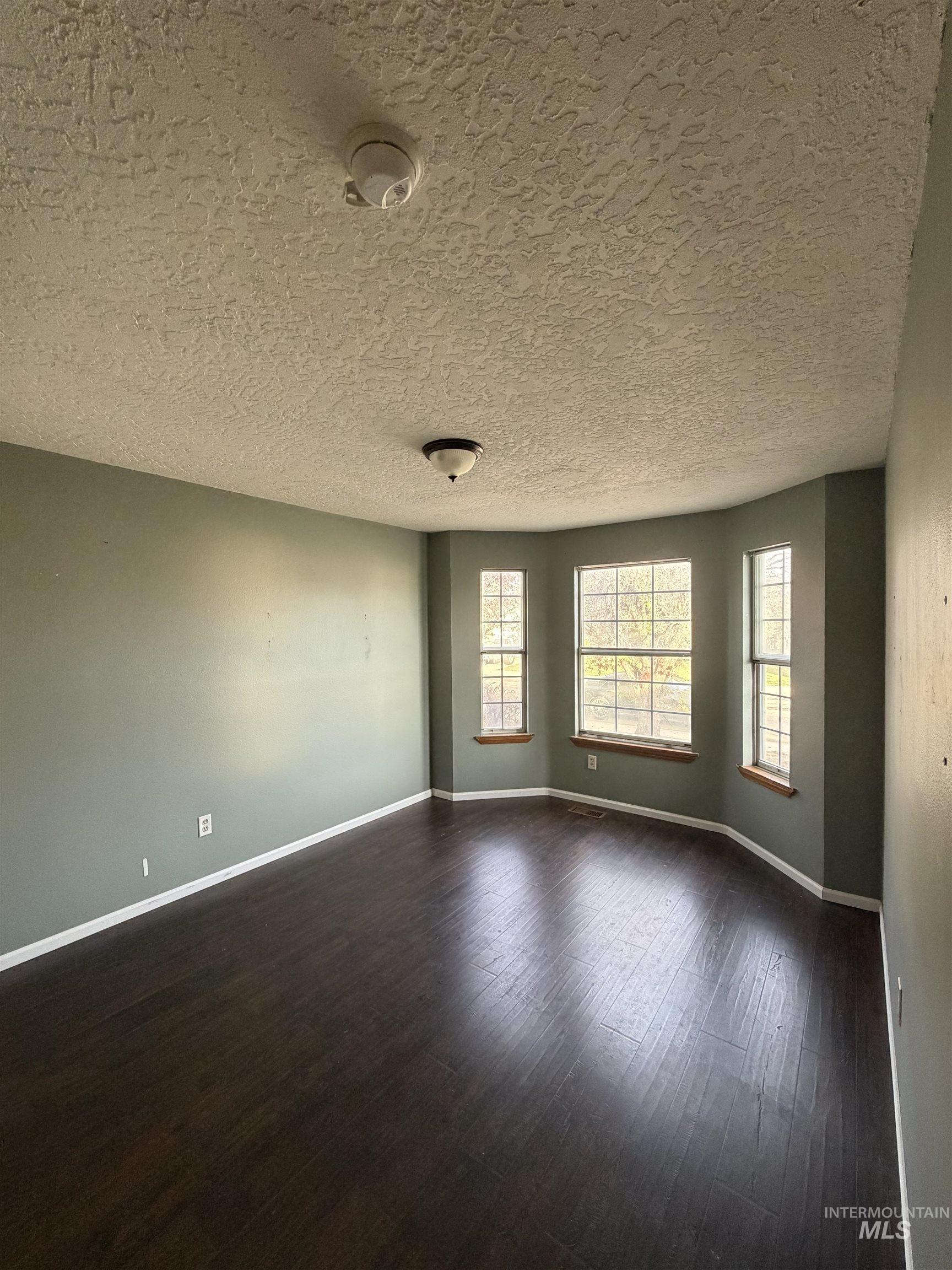Empty room featuring a textured ceiling and dark wood-type flooring